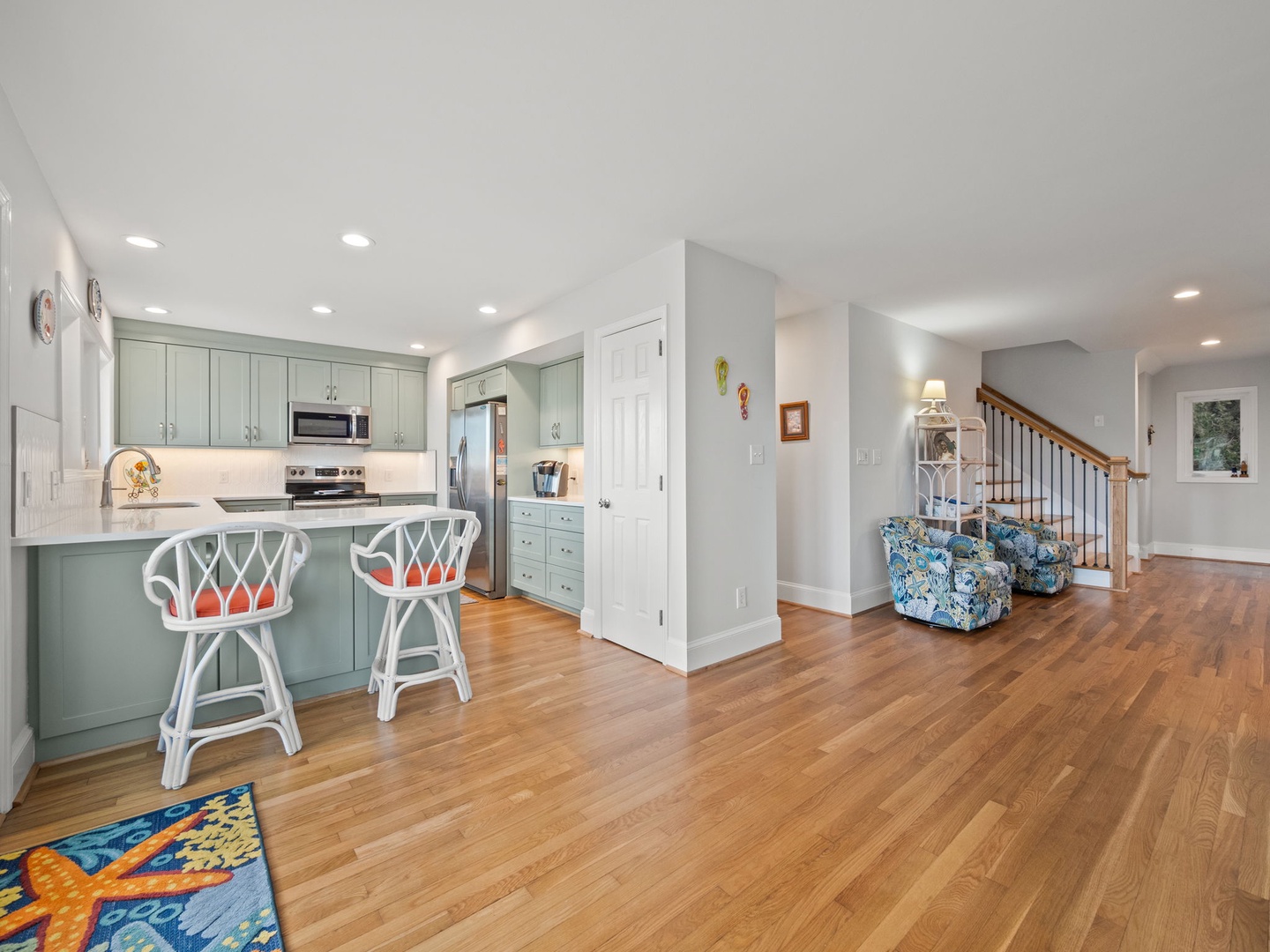 Your open-concept kitchen flows seamlessly into the living area, featuring sage green cabinets and gleaming hardwood floors throughout.