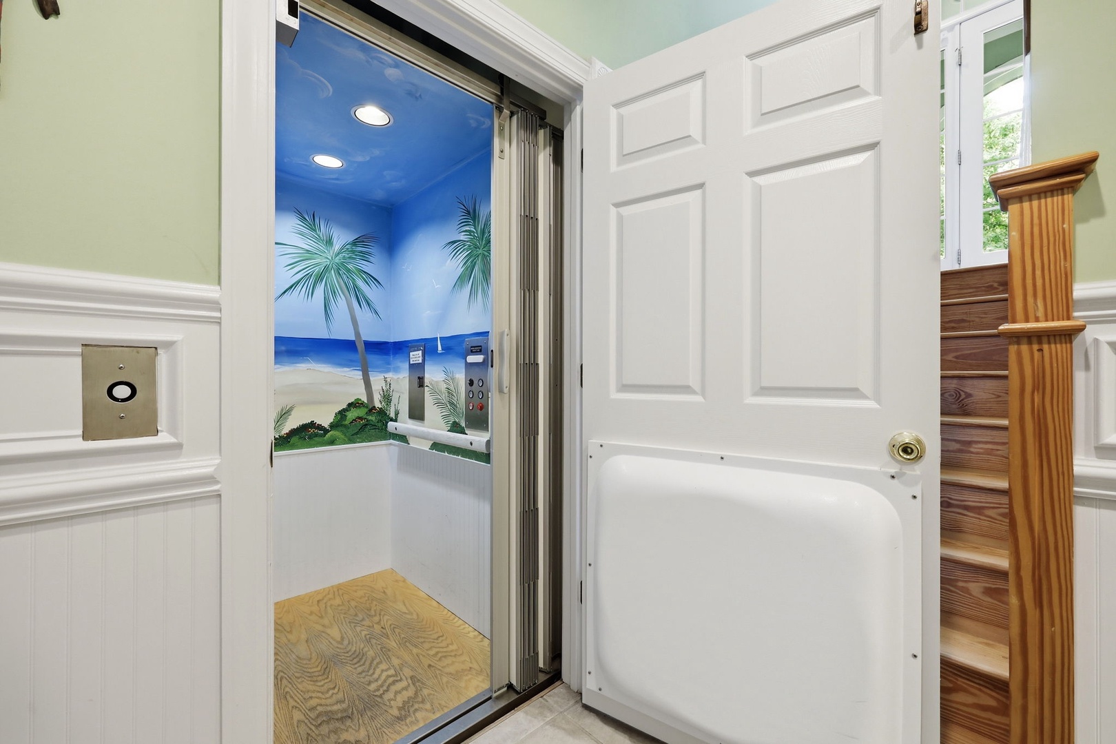 A residential elevator with beach-themed tropical mural offers convenient accessibility between floors in this coastal vacation home.