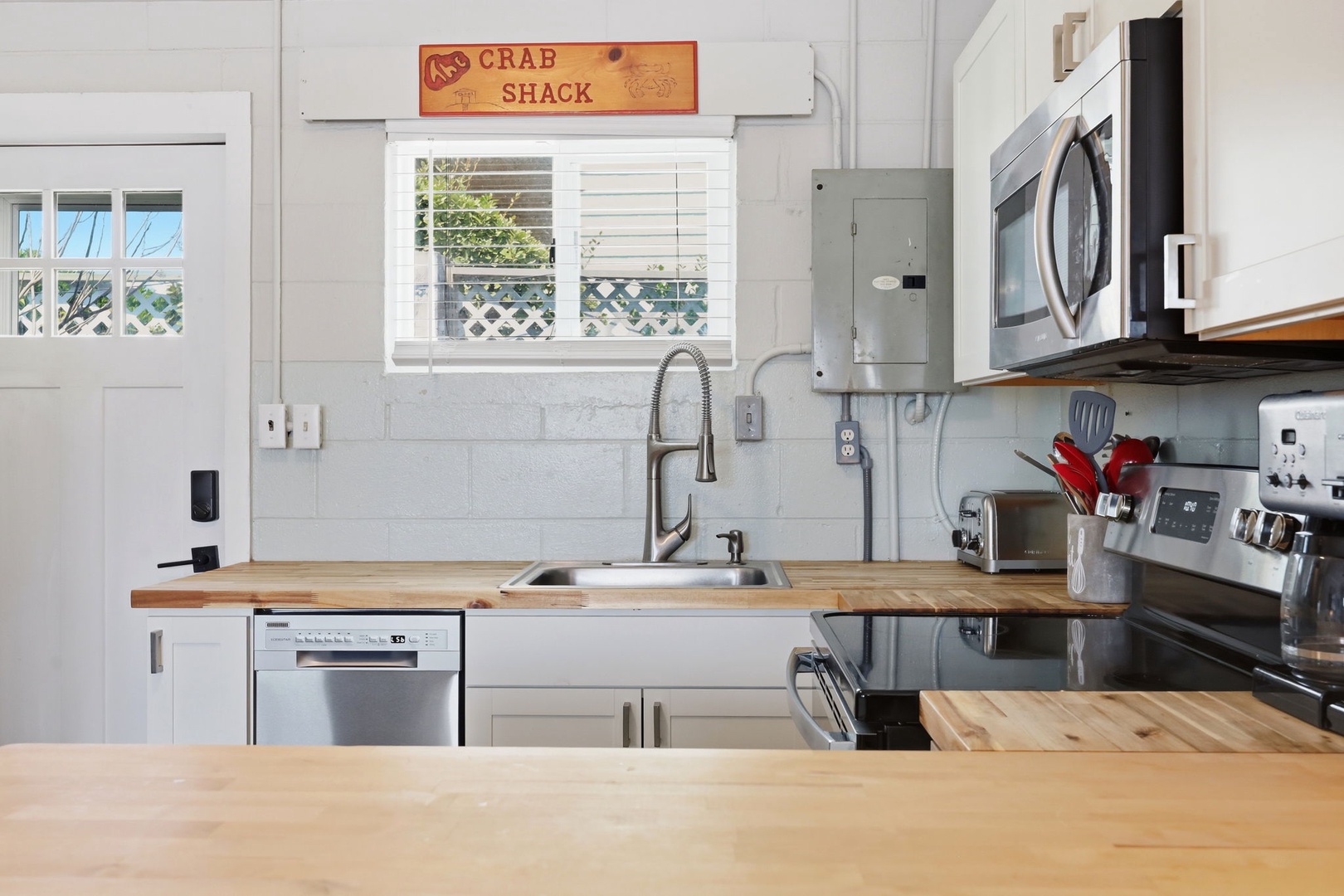 Your fully equipped kitchen features modern appliances, butcher-block counters, and charming coastal character with a cheerful 'Crab Shack' sign overhead welcoming you to cook and gather.