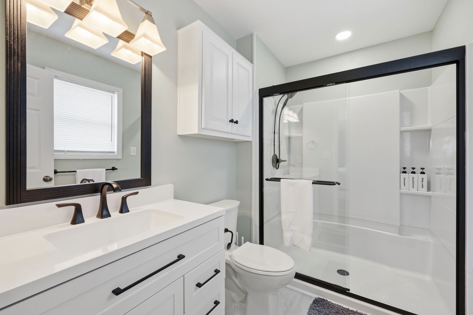 Step into a spotless bathroom with modern fixtures, soft lighting, and a spacious walk-in shower. White cabinetry offers plenty of storage, while natural light from the window enhances your morning routine.