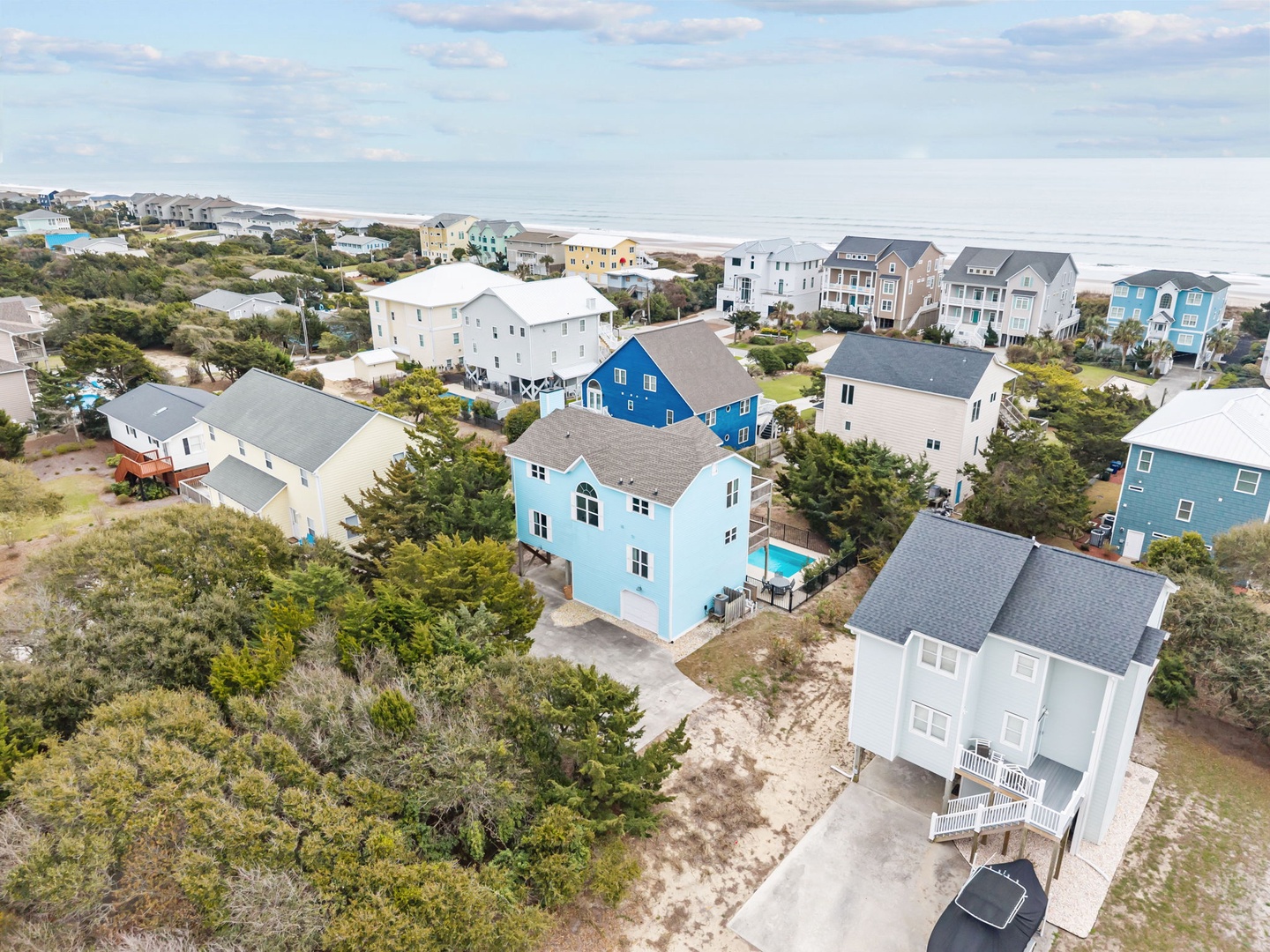 Aerial view of a charming coastal neighborhood with colorful beach houses nestled among natural vegetation near the shoreline.