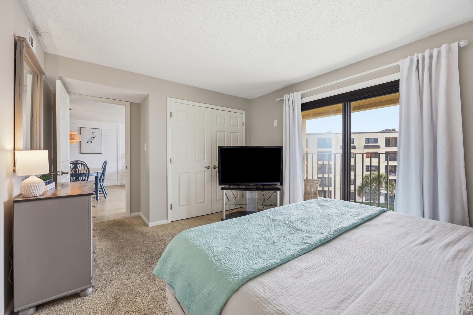 Settle into your serene bedroom where soft linens and calming coastal colors invite relaxation, while your private balcony frames peaceful city views beyond crisp white curtains.