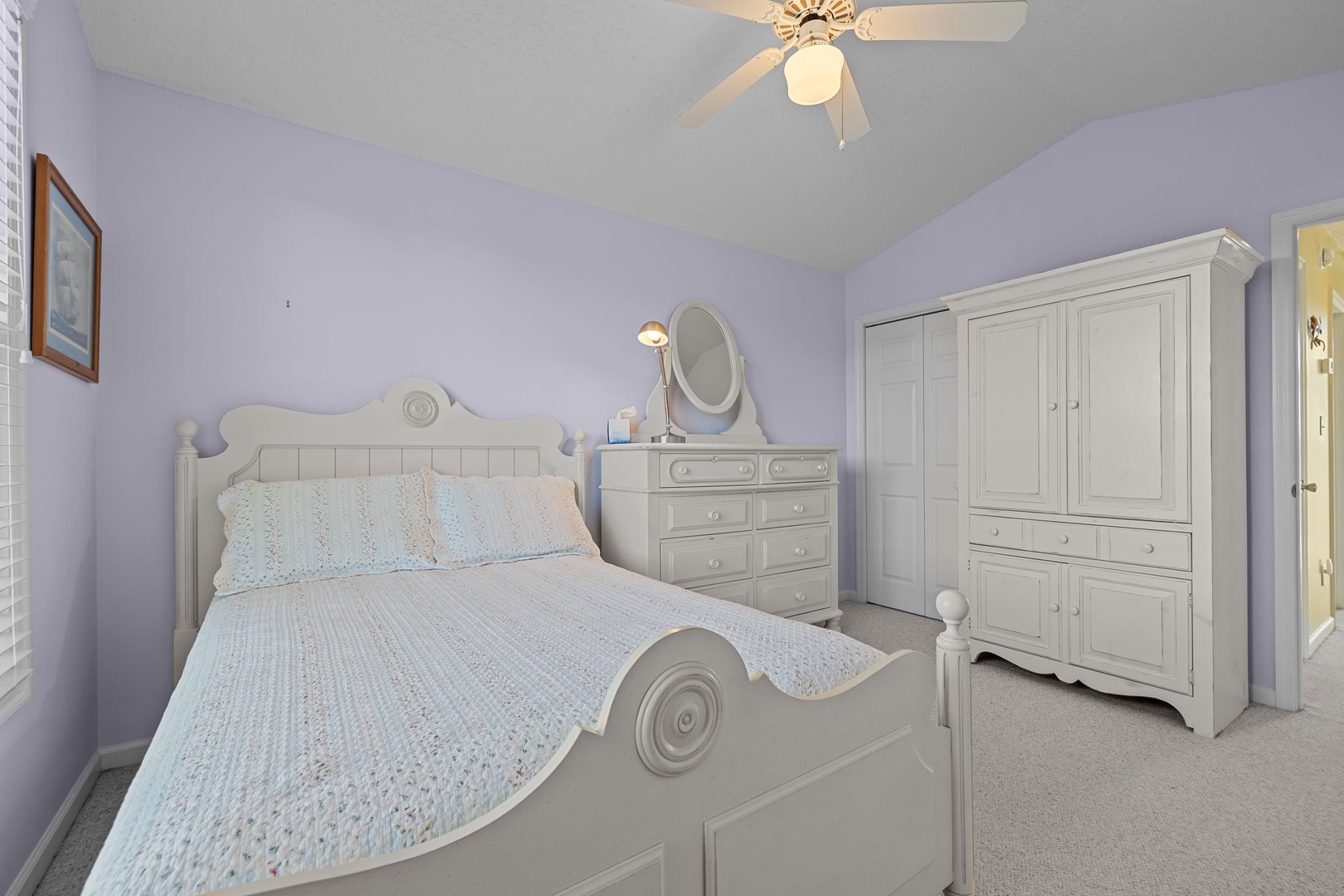 Rest peacefully in this serene lavender bedroom with charming white furnishings, ceiling fan, and ample storage for your belongings.