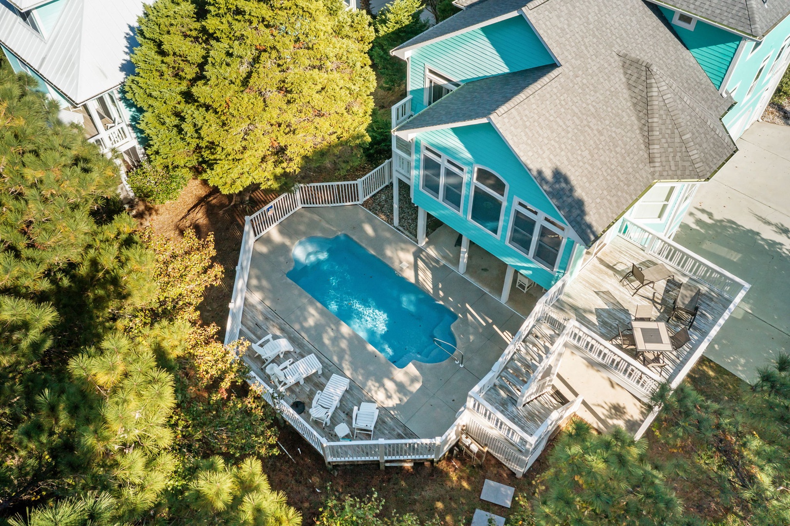 Aerial view of a vibrant turquoise beach house surrounded by lush landscaping and featuring a private swimming pool with multi-level deck areas.