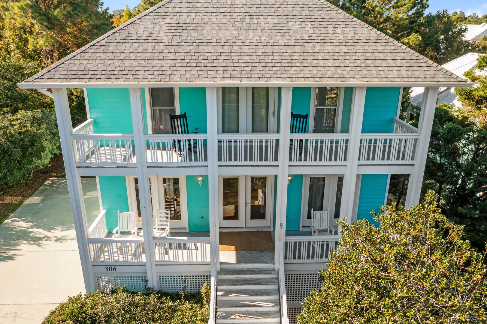 Charming beach cottage with vibrant turquoise shutters and wraparound porches, nestled among lush coastal greenery.