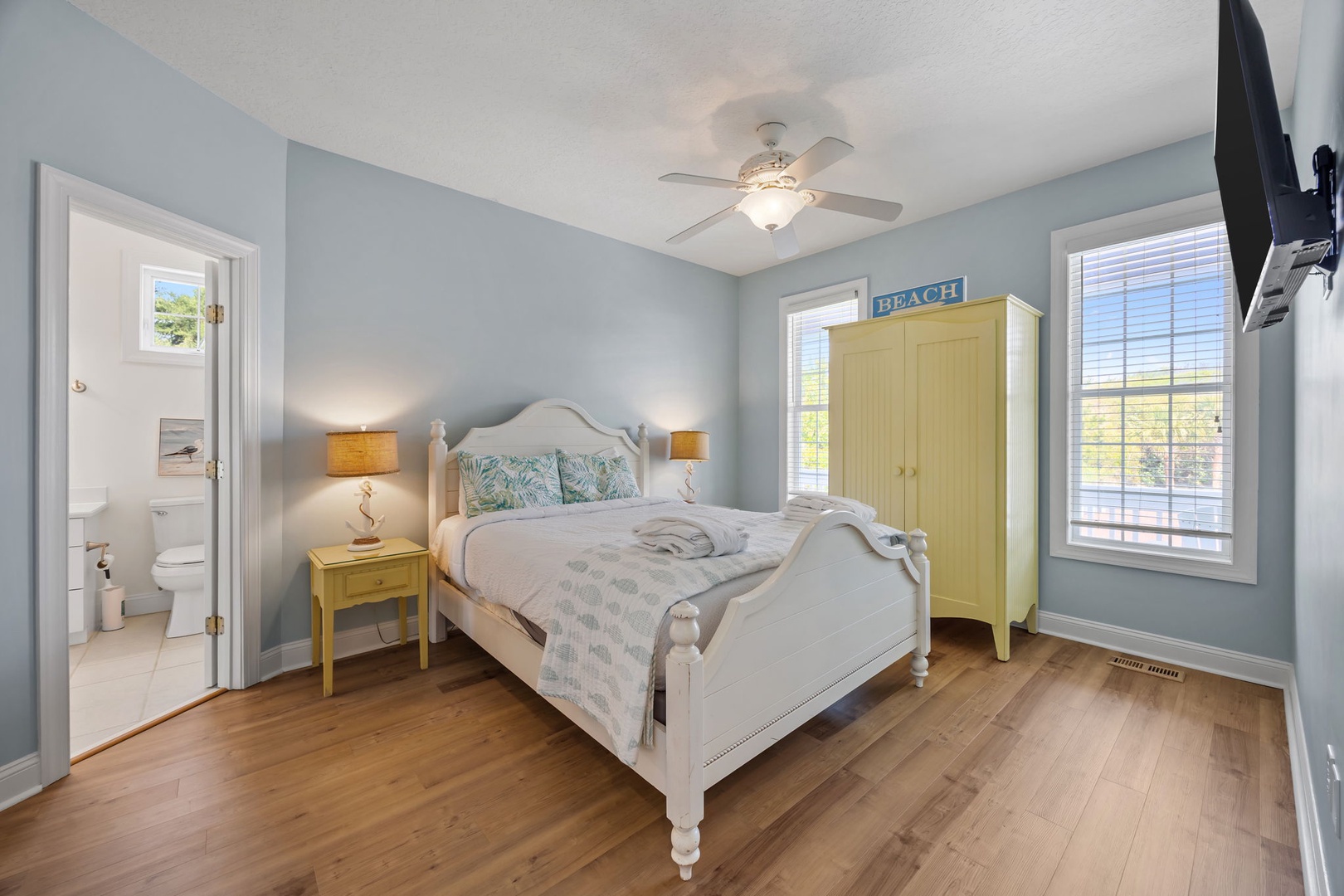 Drift off in your serene coastal bedroom featuring soft blue walls, gleaming hardwood floors, and charming beachy touches throughout.