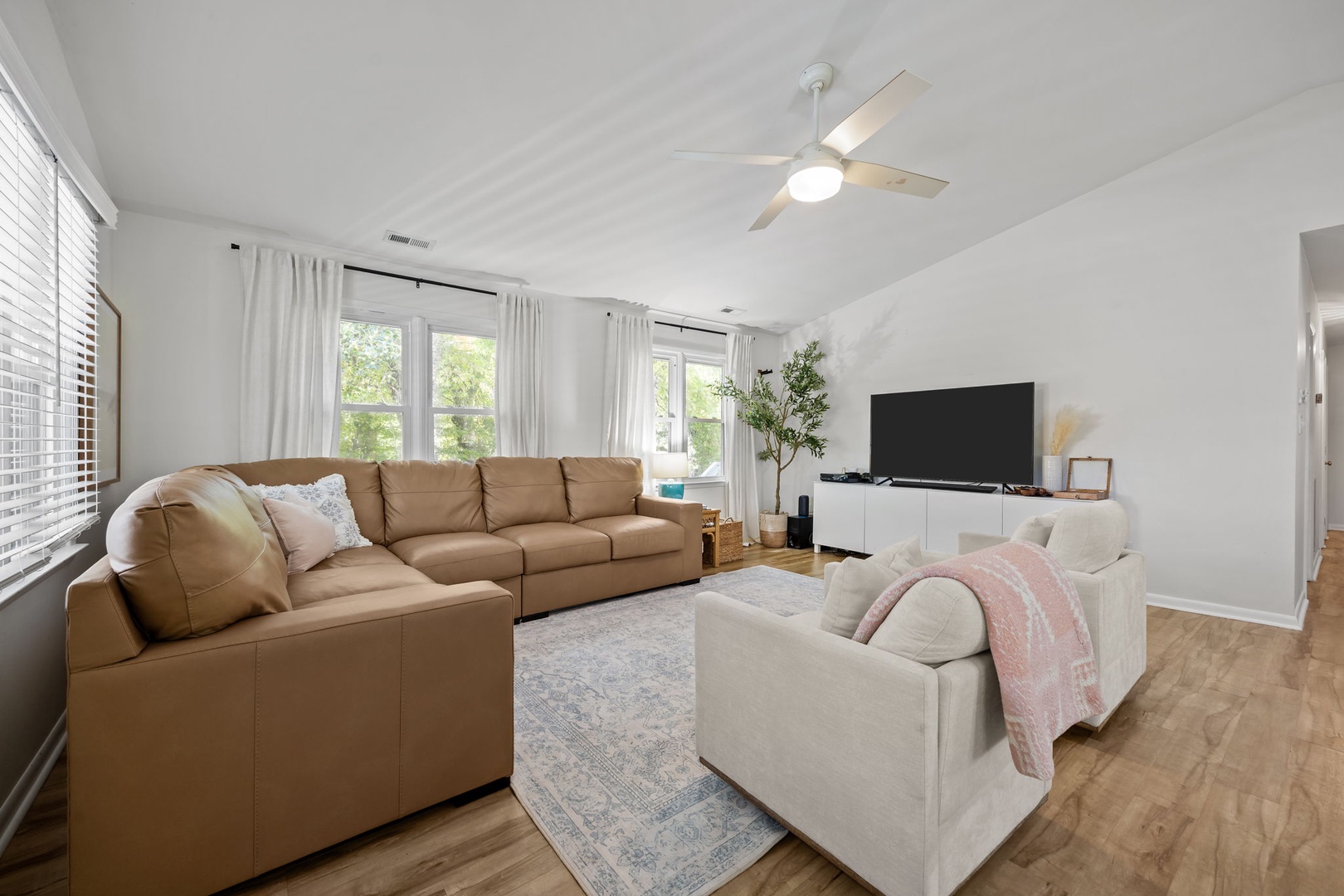 Relax in your bright, open living room with plush seating, modern entertainment center, and ceiling fan keeping you comfortable all day.