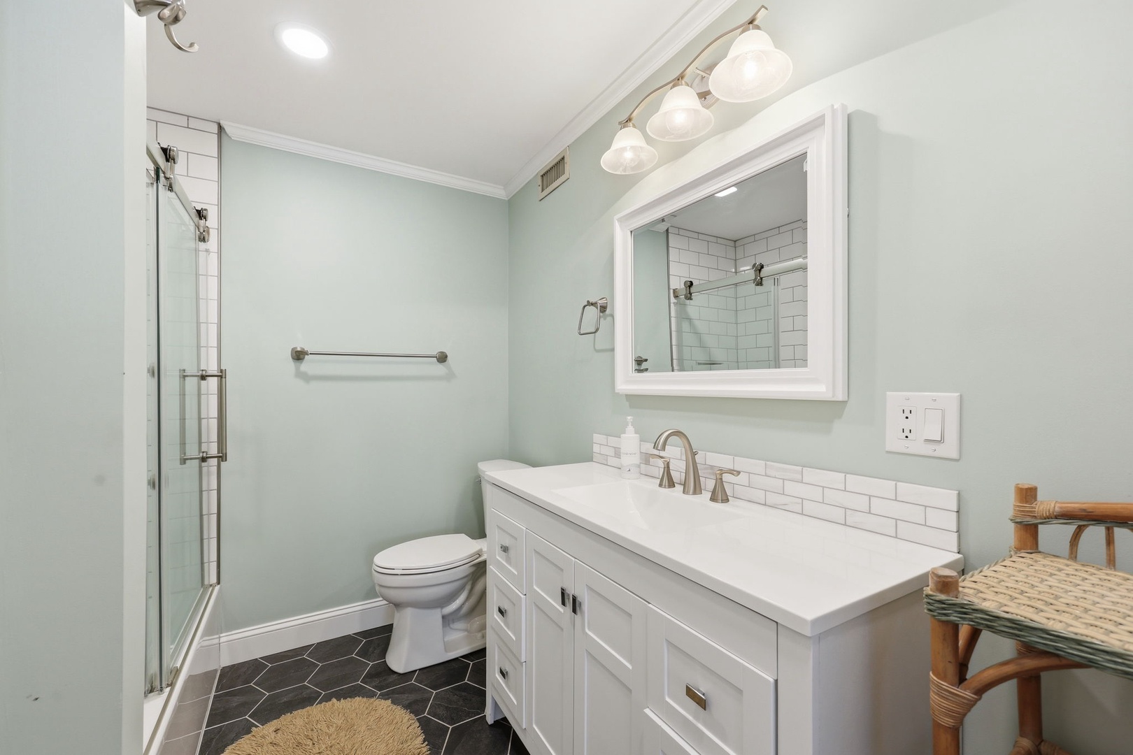 Step into your beautifully renovated bathroom featuring soft mint walls, crisp white subway tile, and a sleek glass-enclosed shower. The spacious vanity provides plenty of room to refresh and unwind after a day of exploring.