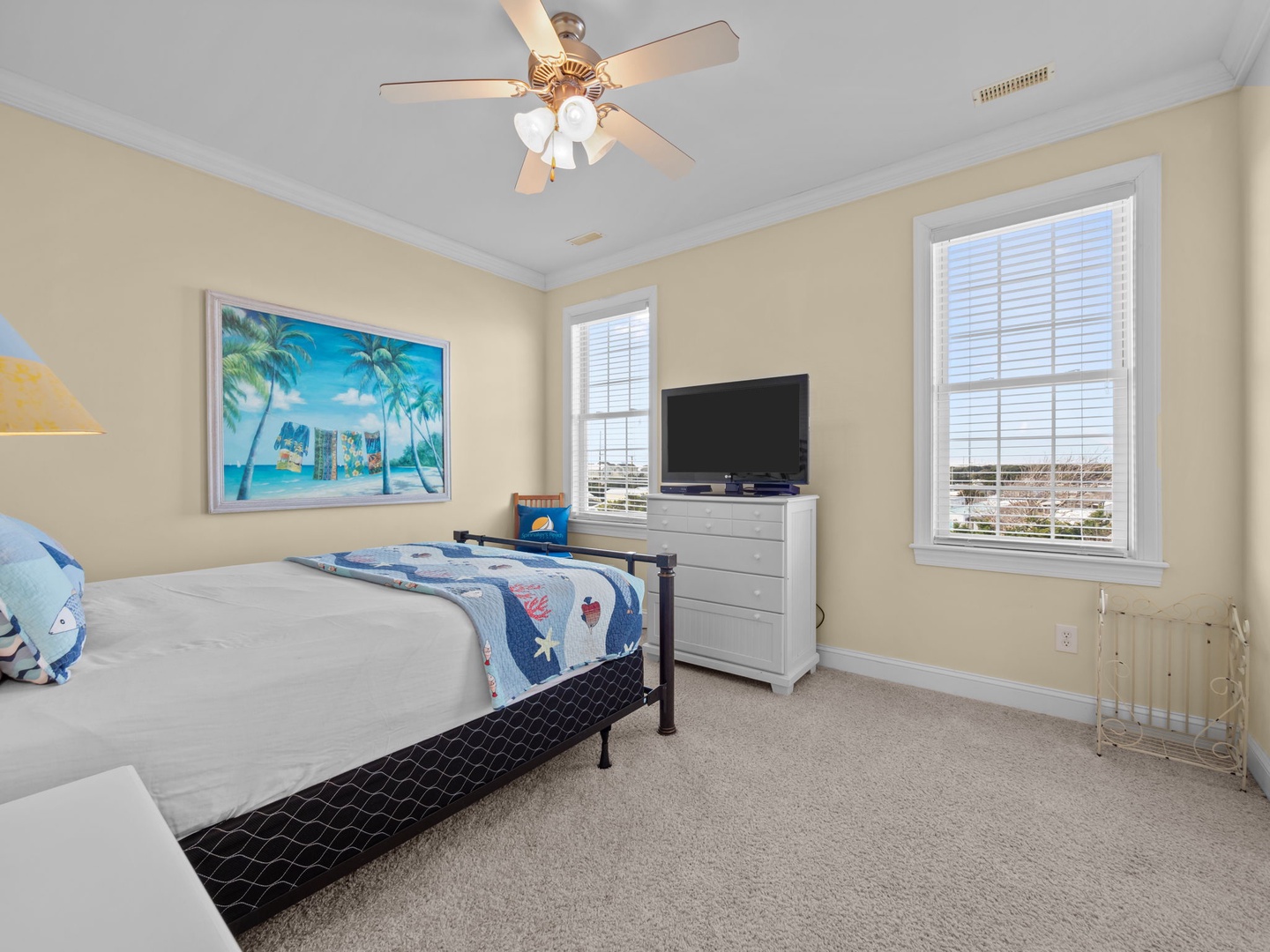 Drift off in this bright bedroom with ocean artwork, TV, and ceiling fan for your comfort.