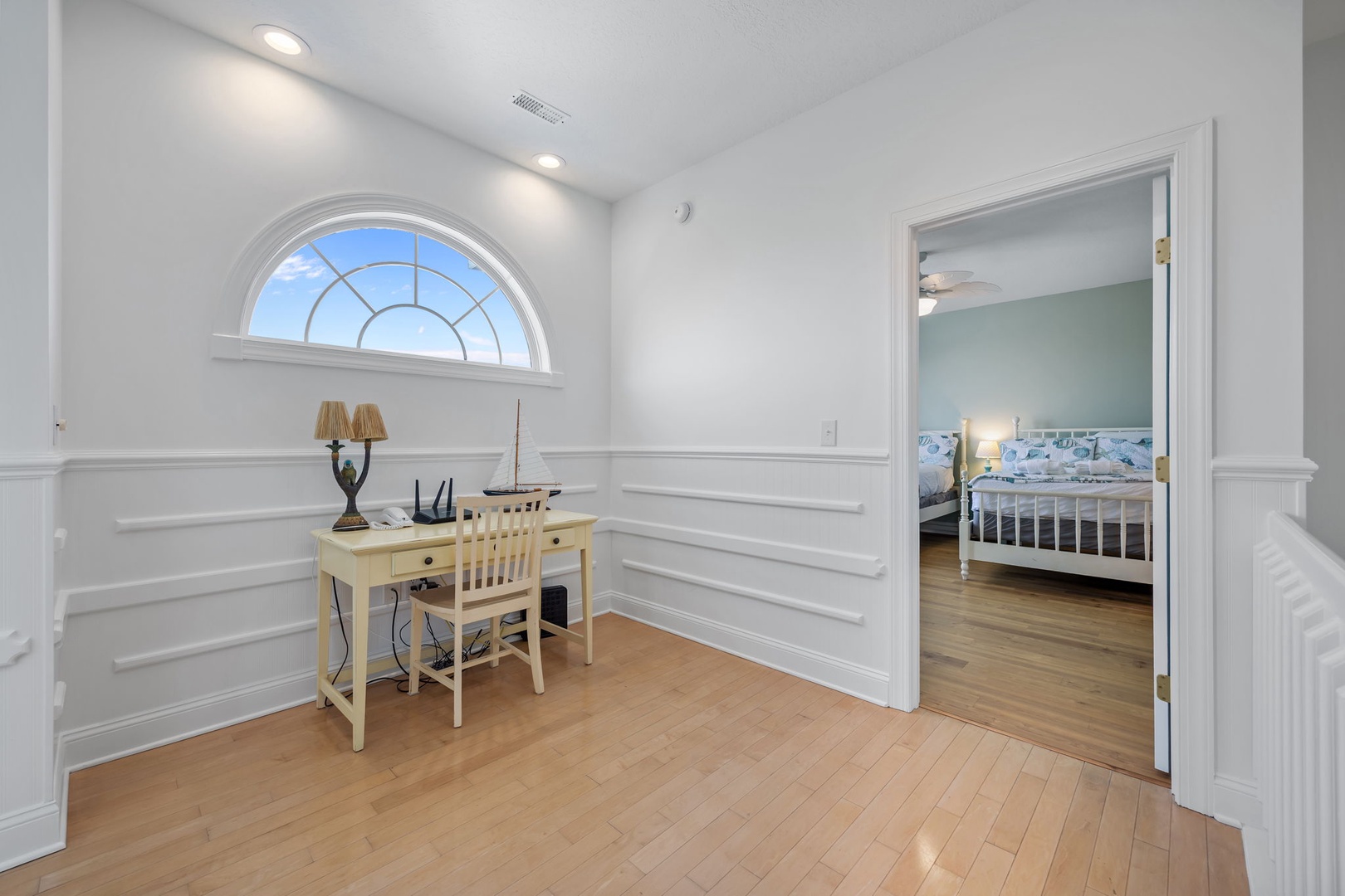 Your bright workspace awaits with elegant wainscoting, an arched window, and polished hardwood floors perfect for peaceful productivity.