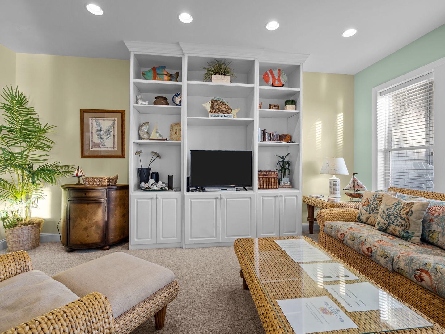 Relax in this bright living space featuring coastal charm with wicker furniture, built-in entertainment center, and tropical plants creating your perfect beach getaway.