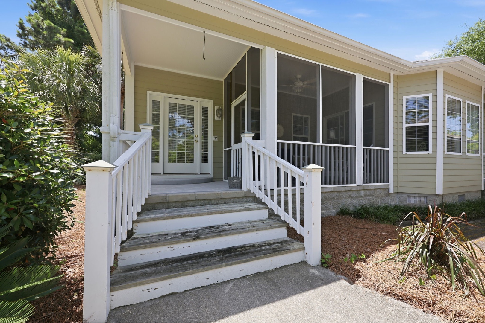 The property entrance features a charming screened porch and white wooden stairs, surrounded by lush tropical landscaping that creates a welcoming arrival experience.
