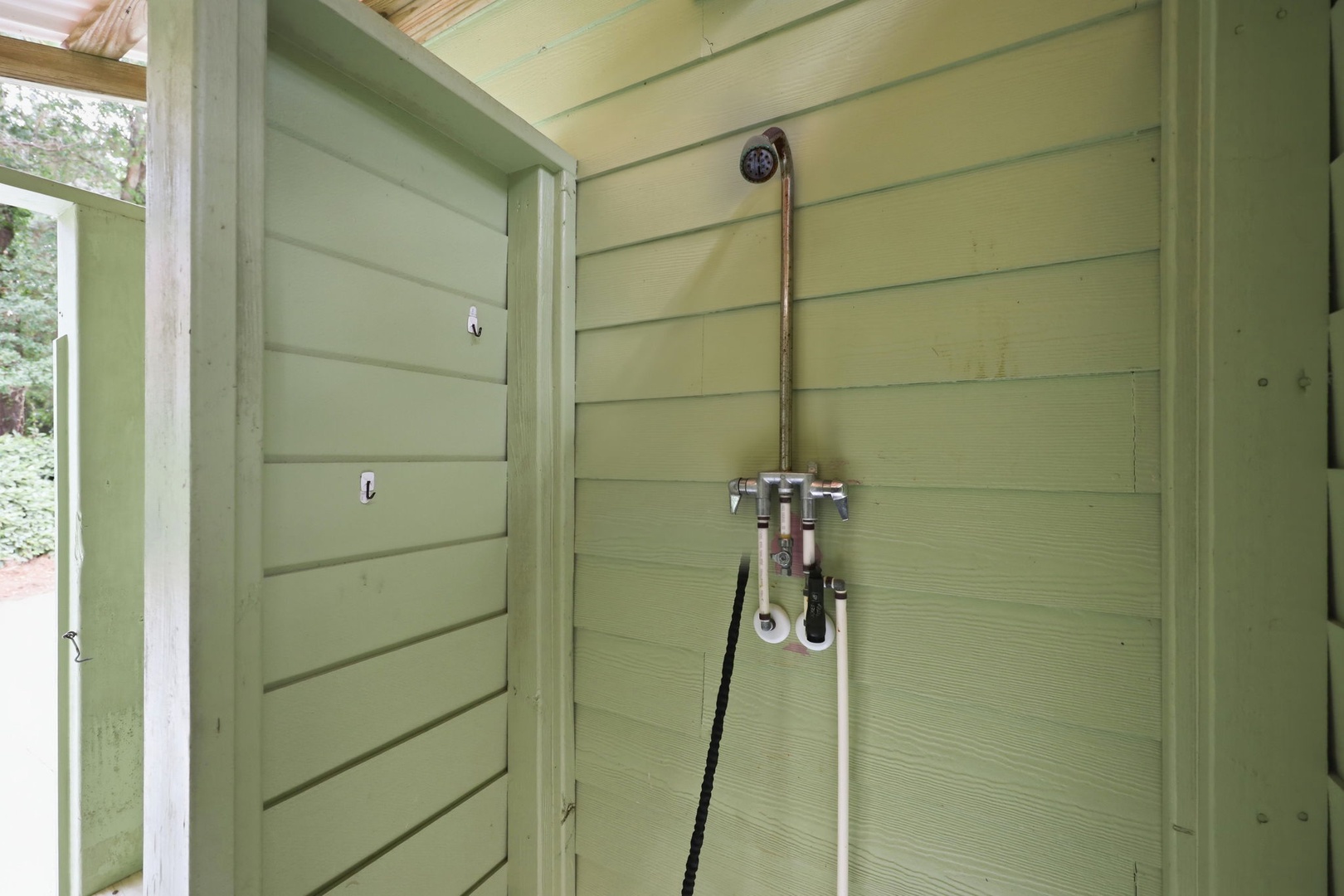 An outdoor shower is surrounded by green wooden paneling. This property includes an accessible outdoor rinse station for refreshing after beach visits or outdoor adventures.