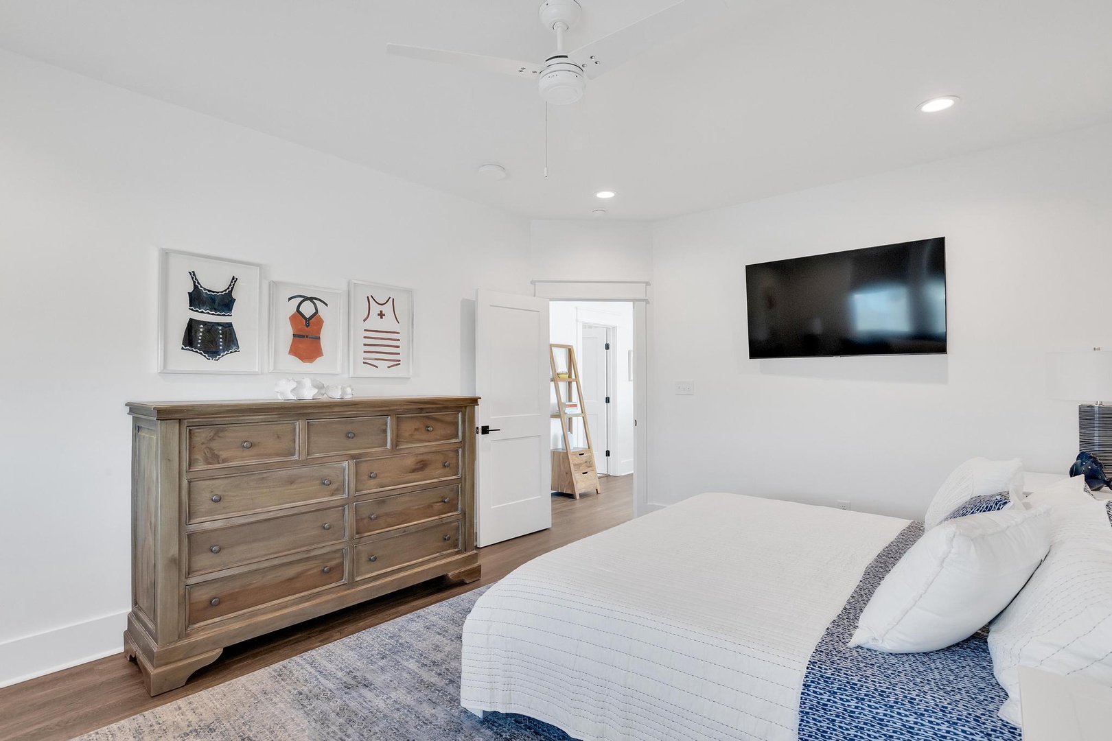 Your bright, serene bedroom awaits with coastal-inspired decor, a plush bed dressed in crisp white linens, and thoughtful touches like a ceiling fan and mounted TV for your comfort.
