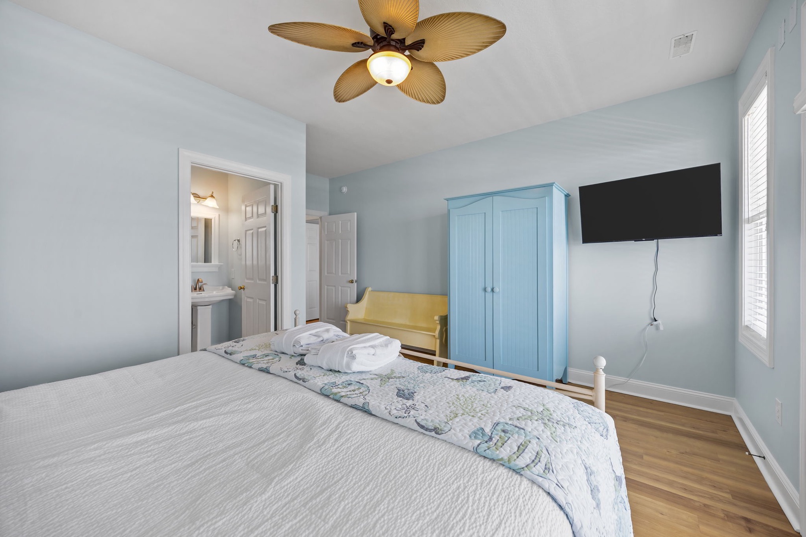 Rest peacefully in your serene bedroom with calming blue walls, a cozy seating nook, and tropical ceiling fan keeping you comfortable.