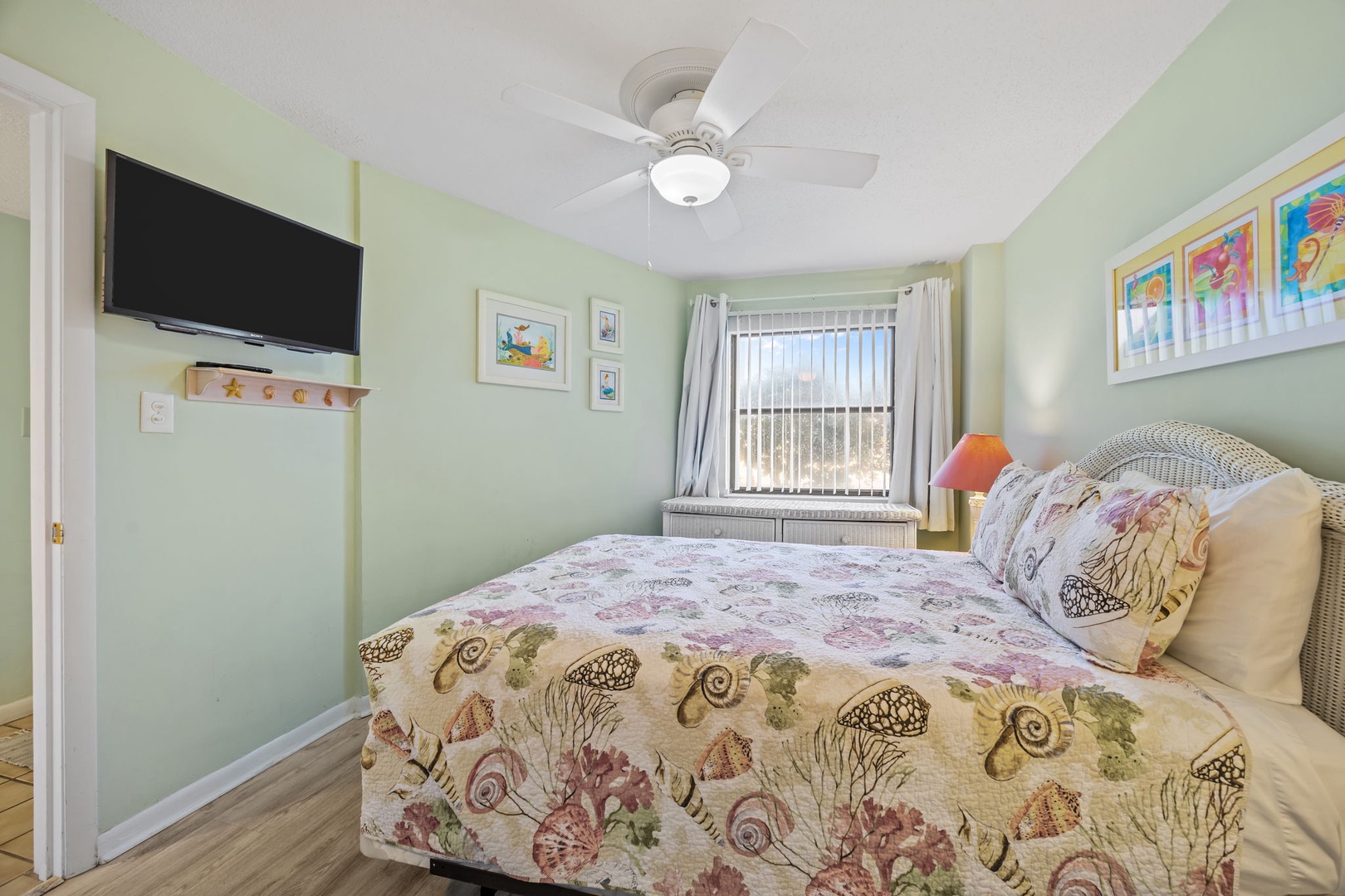 Relax in your coastal bedroom featuring cheerful green walls, seashell-themed bedding, and a ceiling fan for comfort.