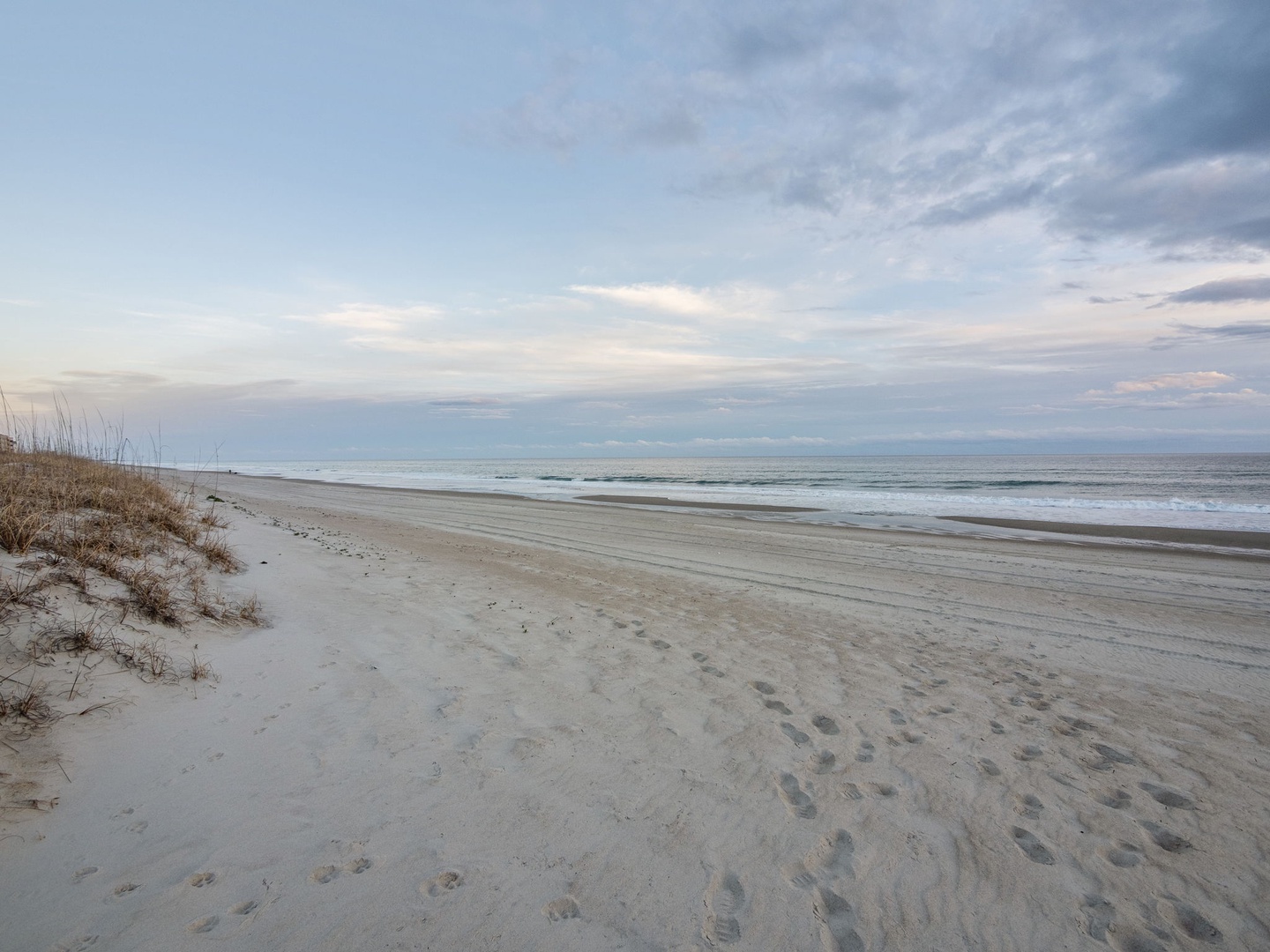 Pristine coastal beach with soft sand dunes and gentle waves under a dramatic cloudy sky.
