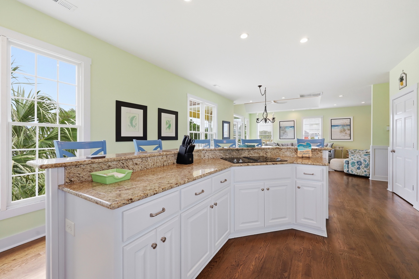 Prepare meals in your sunlit kitchen with granite countertops and white cabinetry, with tropical views through large windows and a welcoming open layout flowing into the living space.