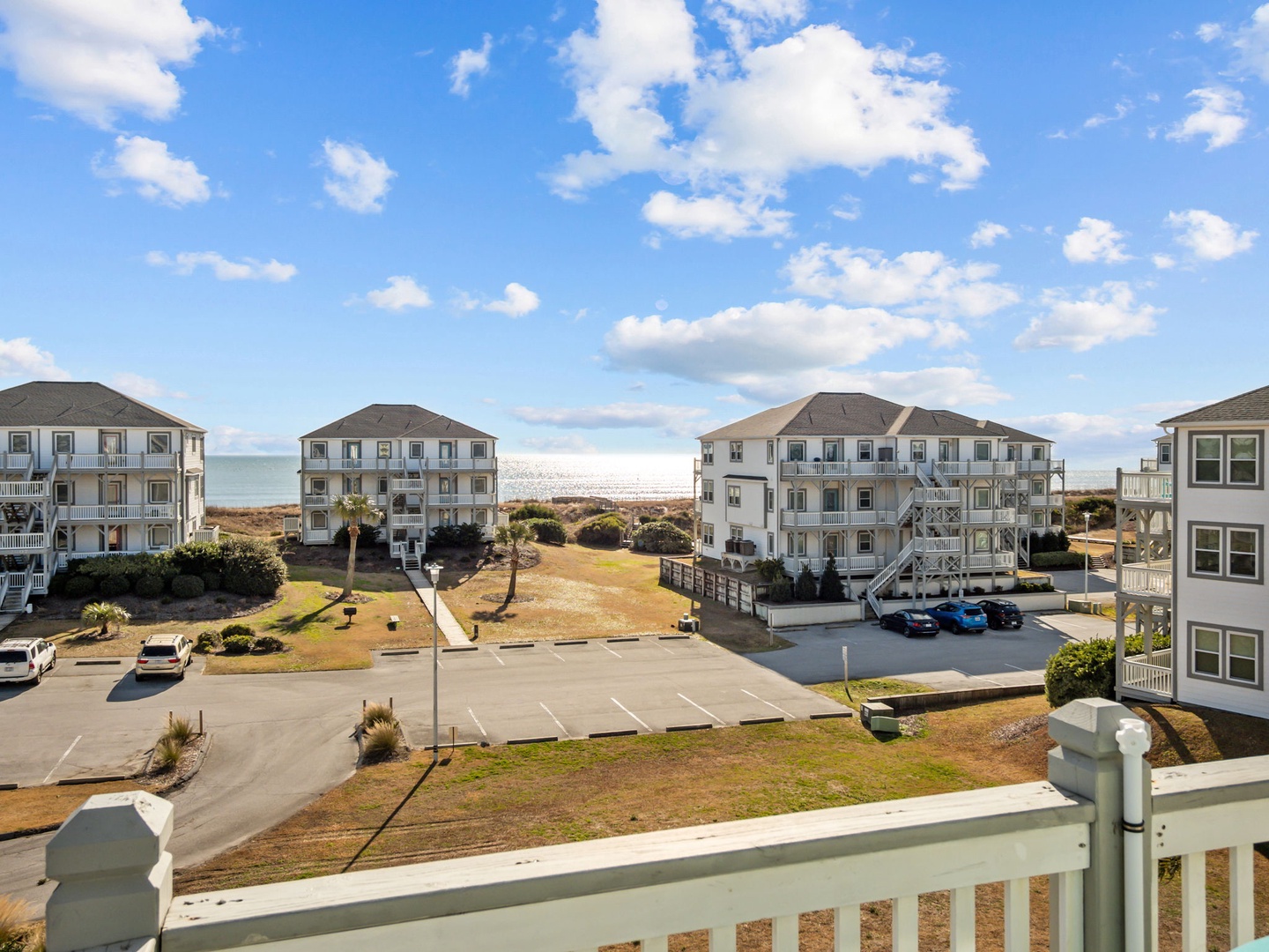 Oceanfront vacation community with multi-story beach houses, parking areas, and direct beach access under bright blue skies.