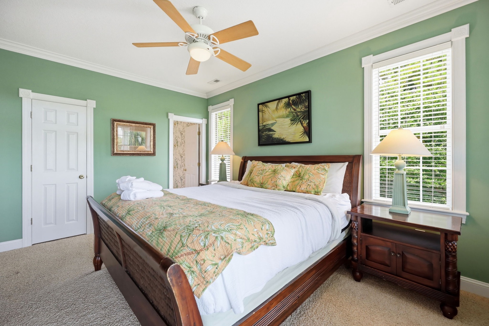 Sink into crisp white linens and tropical comfort in your serene bedroom, where gentle breezes from the ceiling fan and soft natural light create the perfect retreat for restful nights.