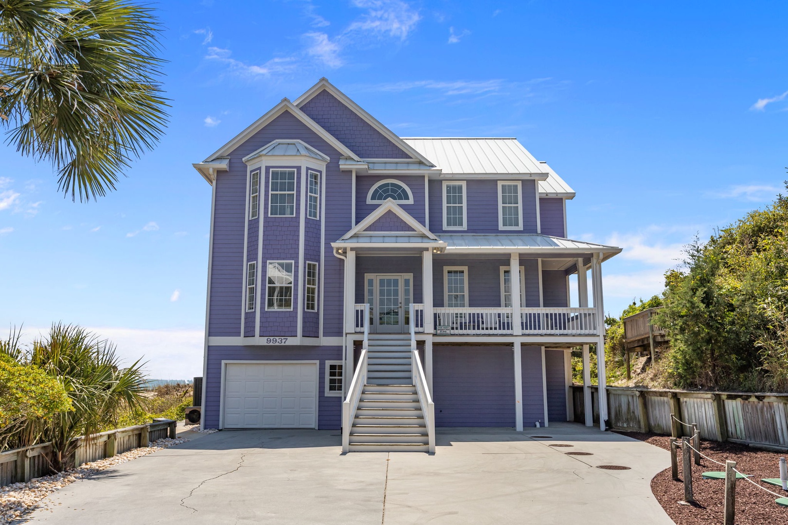 Charming coastal home with wraparound porch and tropical landscaping creates the perfect beach getaway setting.
