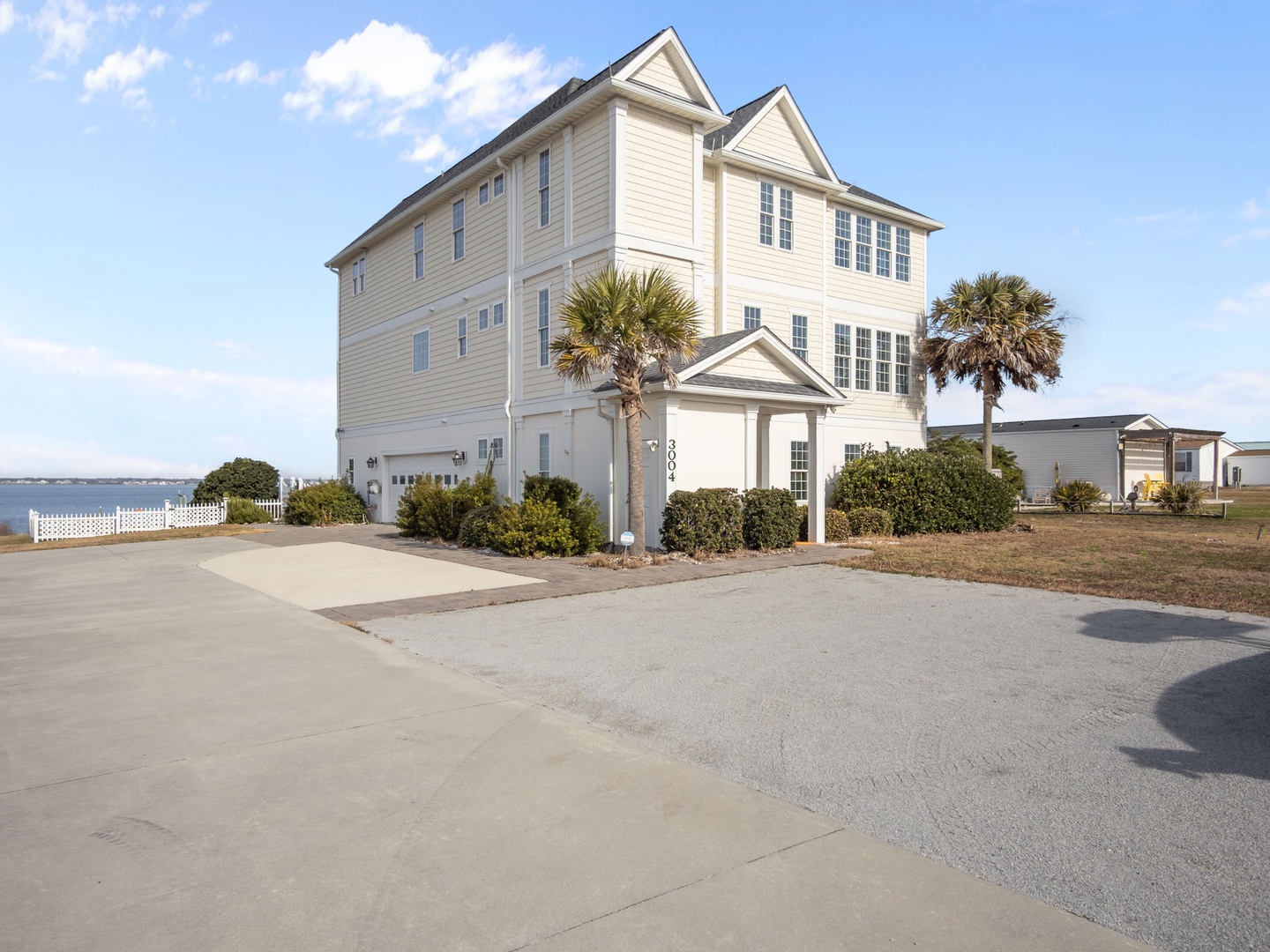 Spacious three-story coastal home with palm trees and ample parking, perfectly positioned in a quiet residential setting.