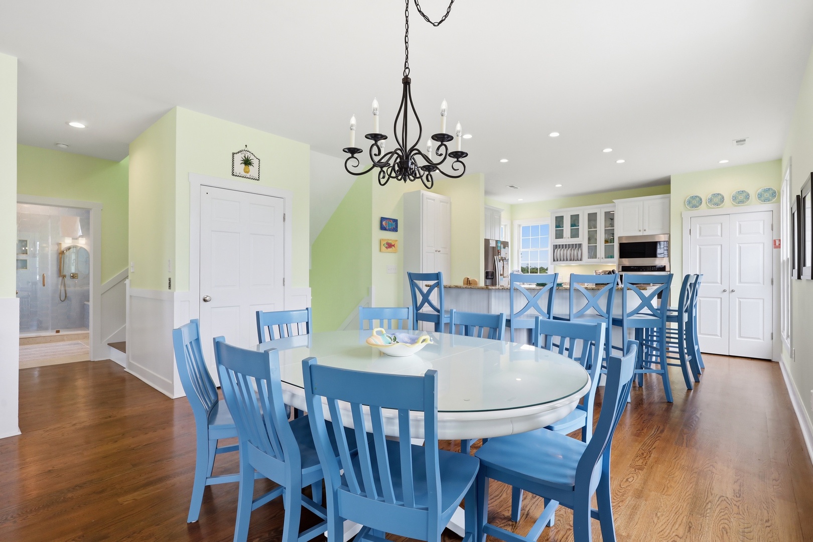 Gather around the spacious dining table with seating for twelve, where laughter flows freely under the warm chandelier glow. The open kitchen invites you to whip up feasts together in this bright, cheerful space.