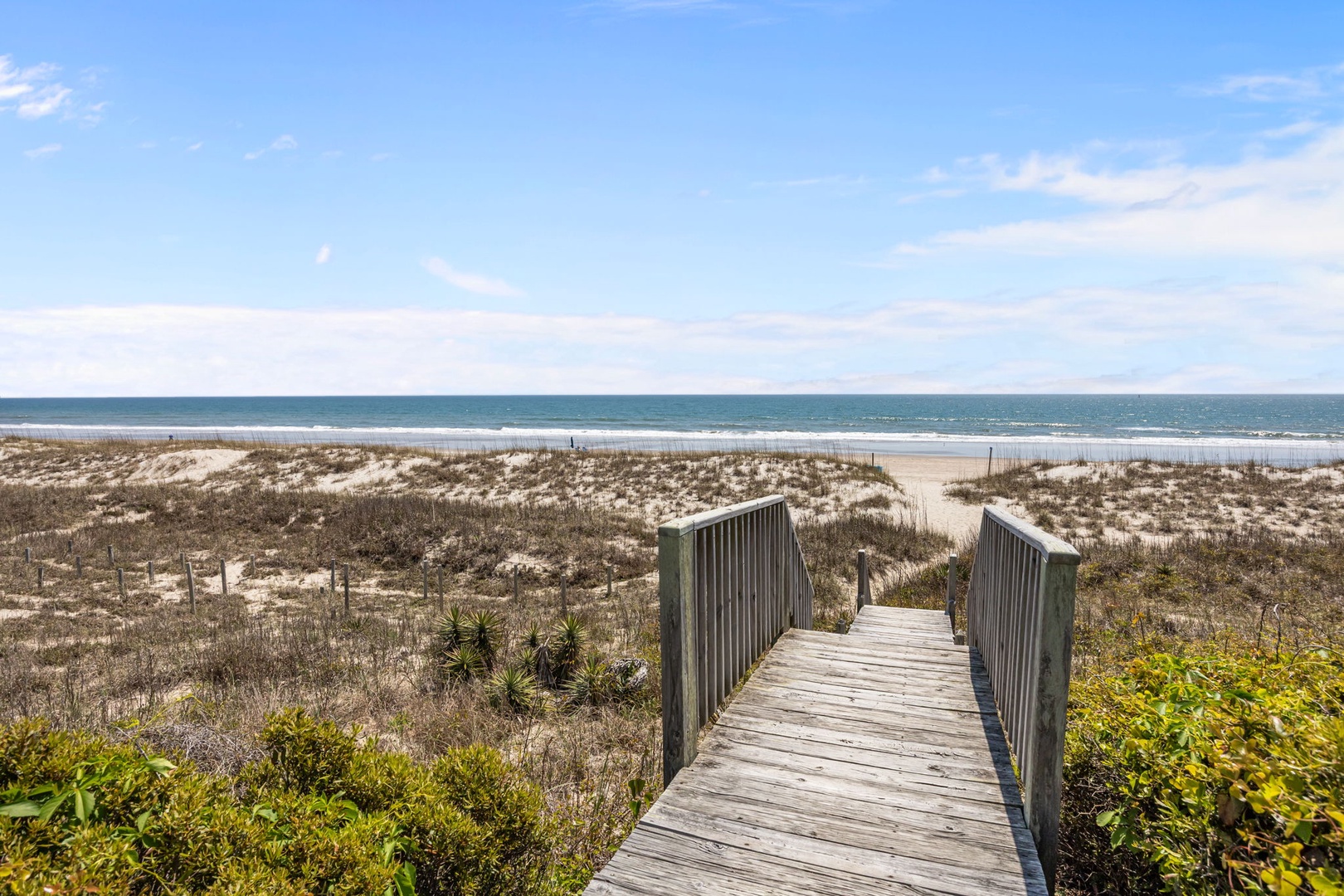 Wooden boardwalk leads through coastal dunes to pristine beach access with ocean views beyond.
