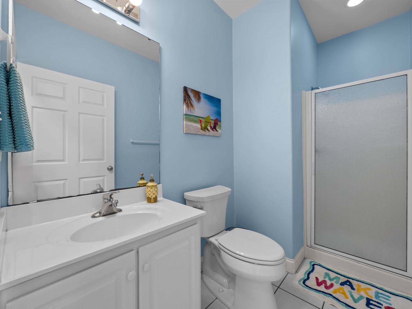 Refresh in your bright coastal bathroom with cheerful blue walls, beach artwork, and tropical touches that make every morning feel like vacation.