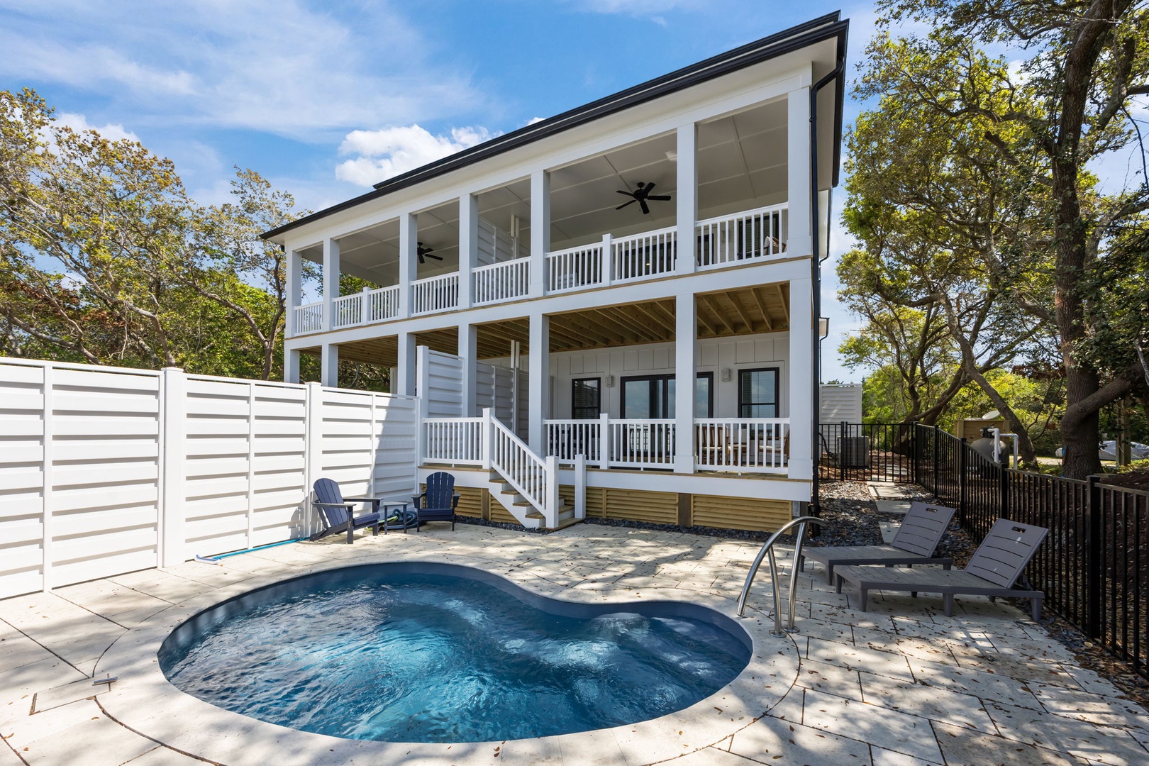 A charming two-story rental home with wraparound porches and private pool, nestled among mature trees in a peaceful residential setting.