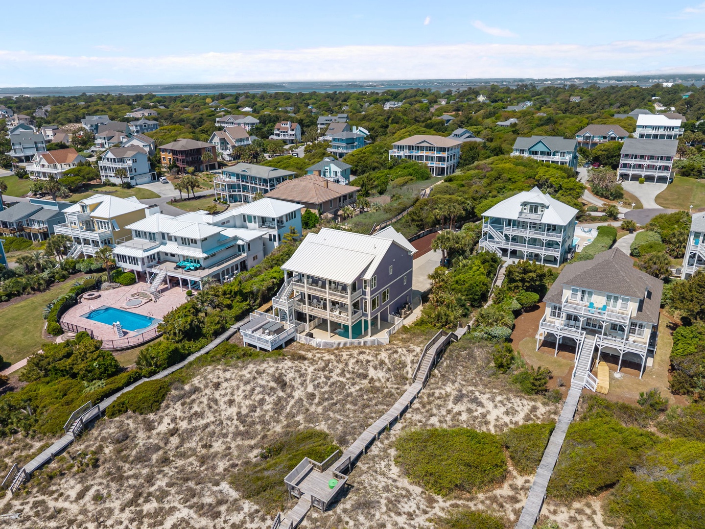 Aerial view of coastal vacation homes nestled among lush vegetation, featuring a mix of traditional and modern architecture with ocean access via wooden boardwalks.