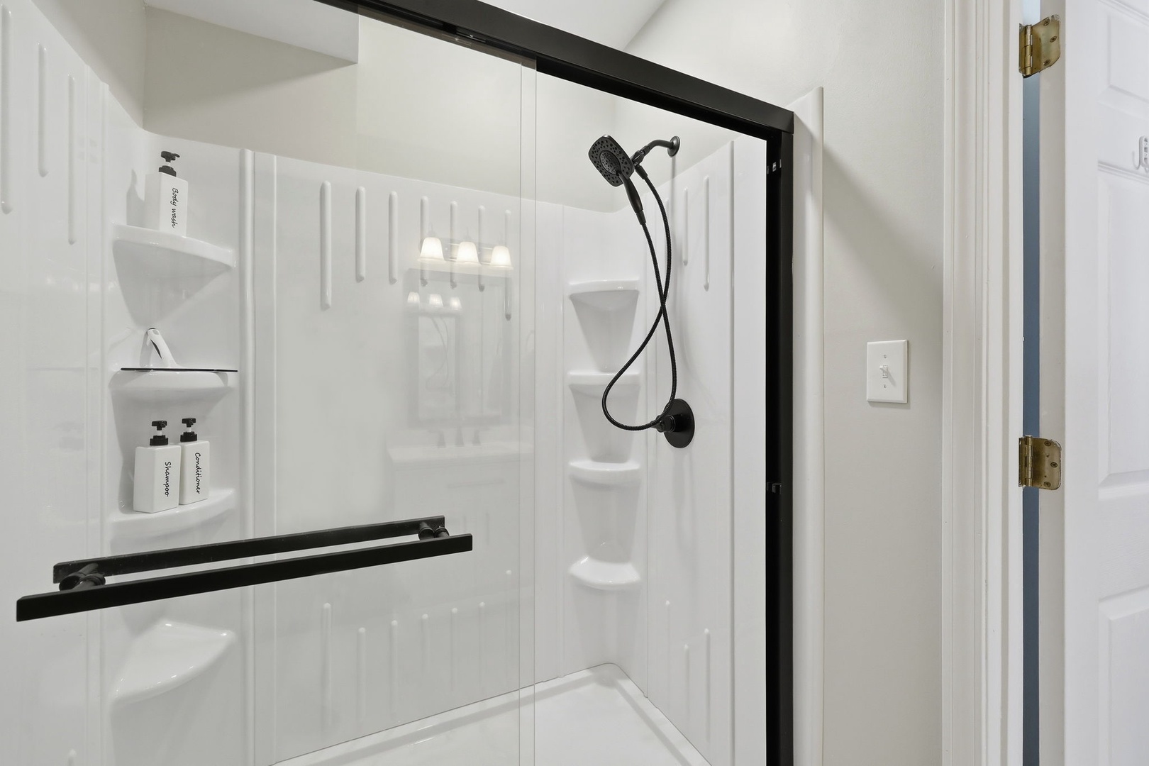 Step into your pristine, modern shower featuring elegant black fixtures, built-in shelving for your essentials, and a rainfall showerhead for a refreshing start to your day.