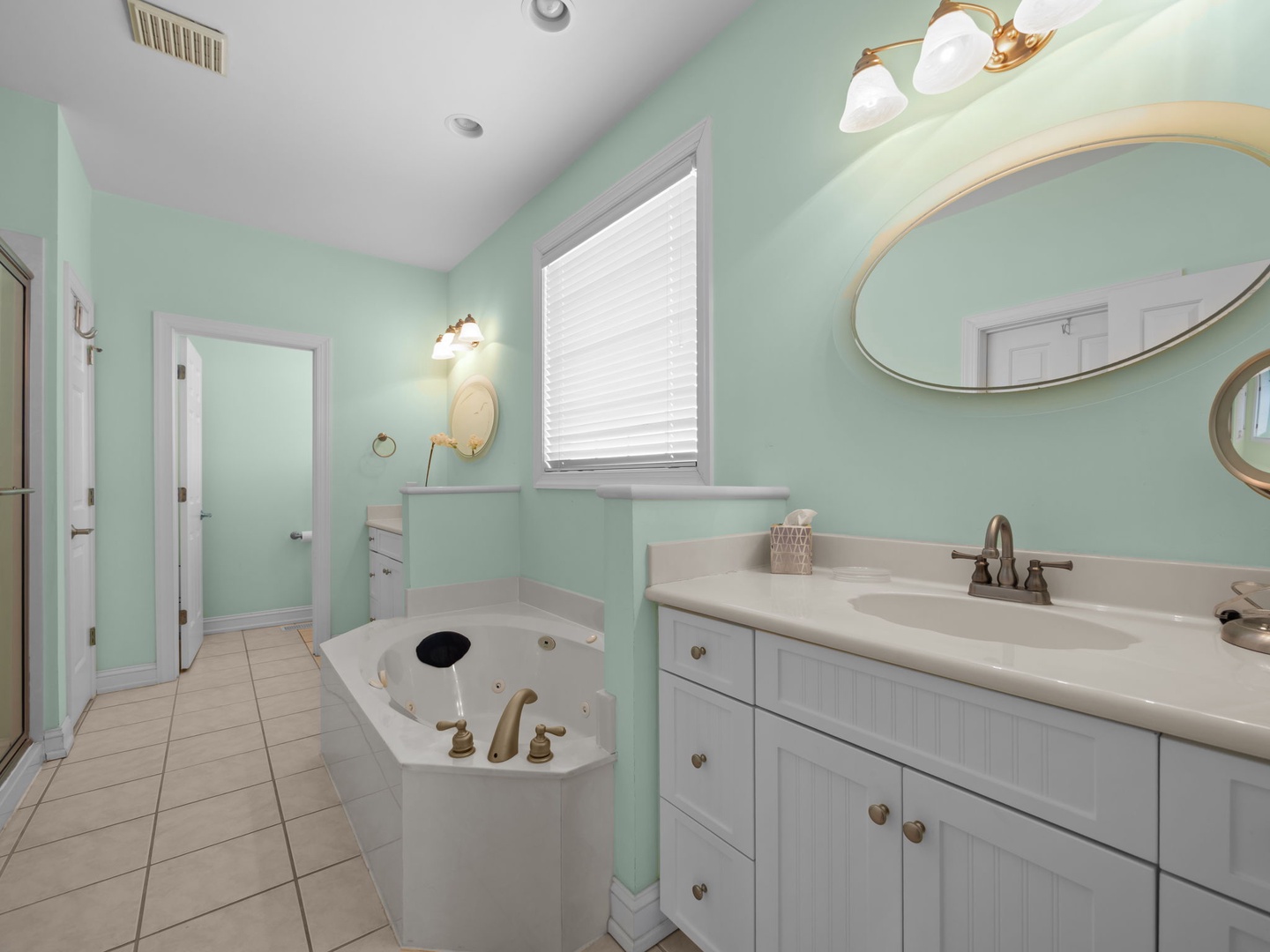 Relax in your spacious bathroom featuring soothing mint green walls, a luxurious soaking tub, and bright natural light streaming through the window.