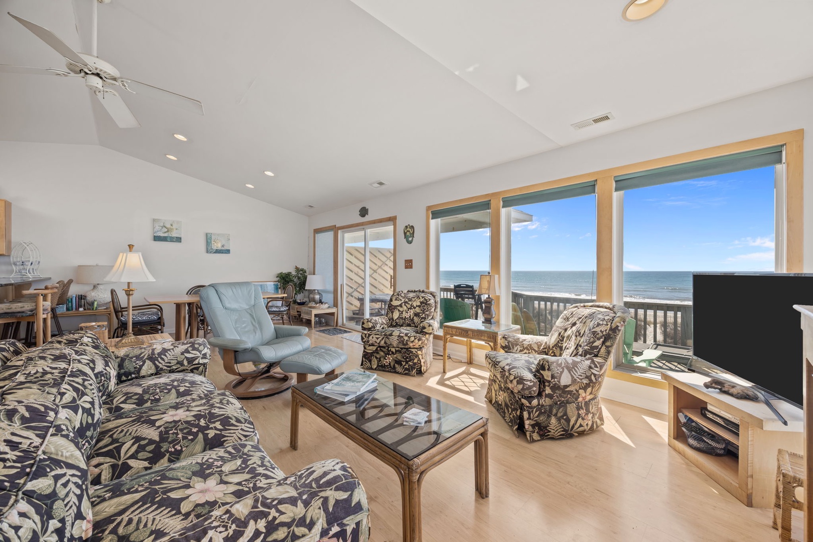 Relax in your bright oceanfront living room where comfortable seating meets stunning sea views through expansive windows.