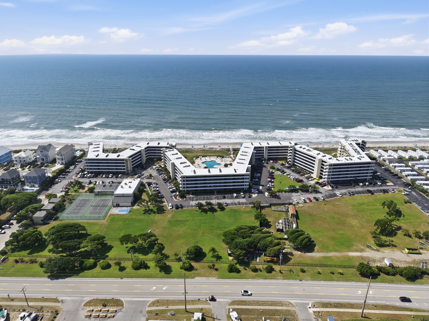 Beachfront property complex featuring multiple mid-rise buildings, swimming pools, tennis courts, and direct ocean access with expansive lawns and parking areas.