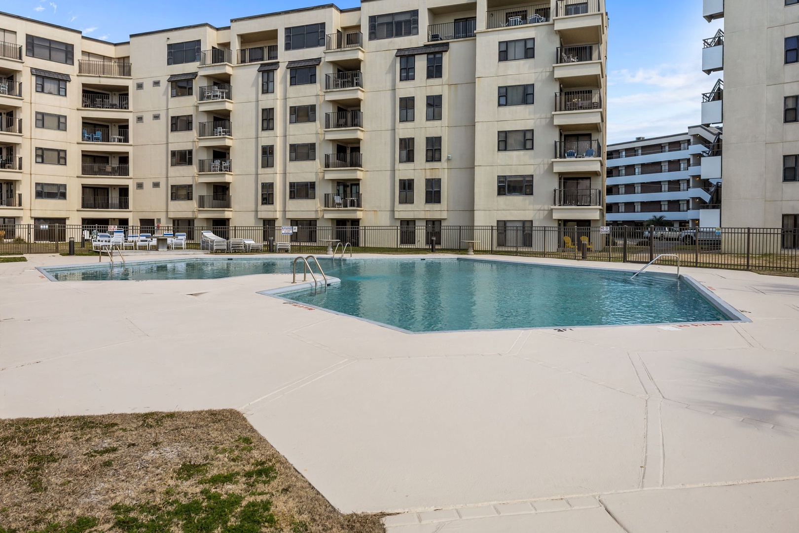 Multi-level property featuring a sparkling outdoor pool surrounded by spacious sundeck and lounge chairs, with modern balconies overlooking the shared aquatic area.
