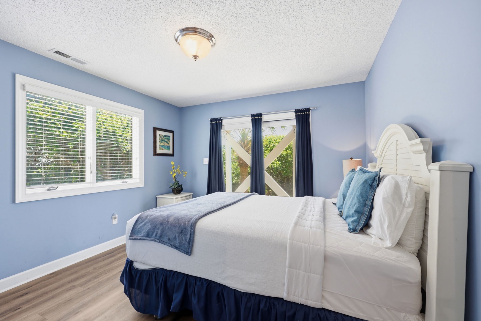 Picture yourself relaxing in this tranquil bedroom, where calming blue walls and crisp white linens create your perfect coastal retreat. Natural light streams through the windows, inviting gentle breezes and views of tropical greenery just outside.