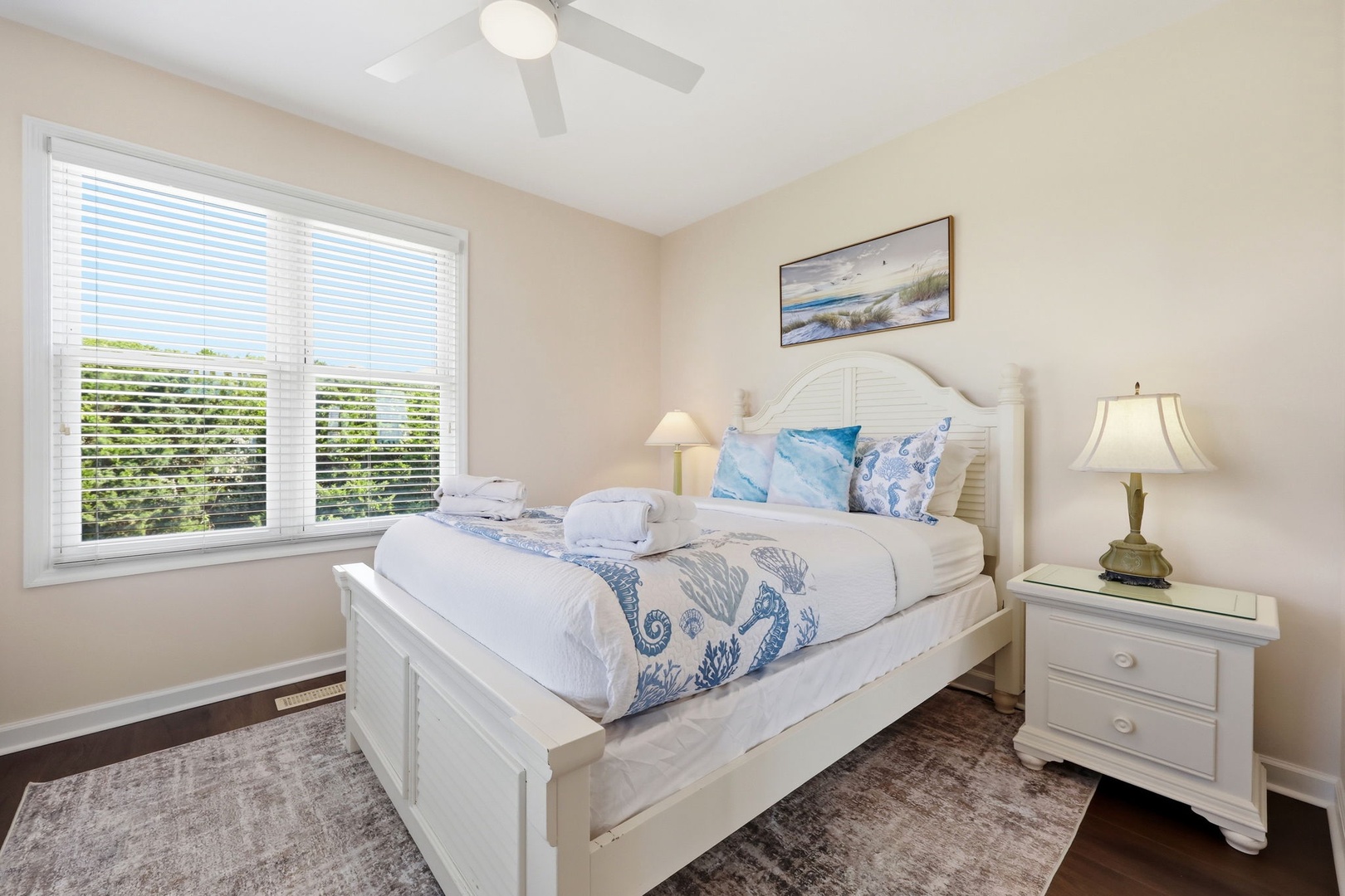 Drift off in this serene coastal-themed bedroom, where soft linens and gentle seaside accents invite your most restful nights. The ceiling fan keeps you cool, while natural light and beach-inspired decor create a calming retreat.