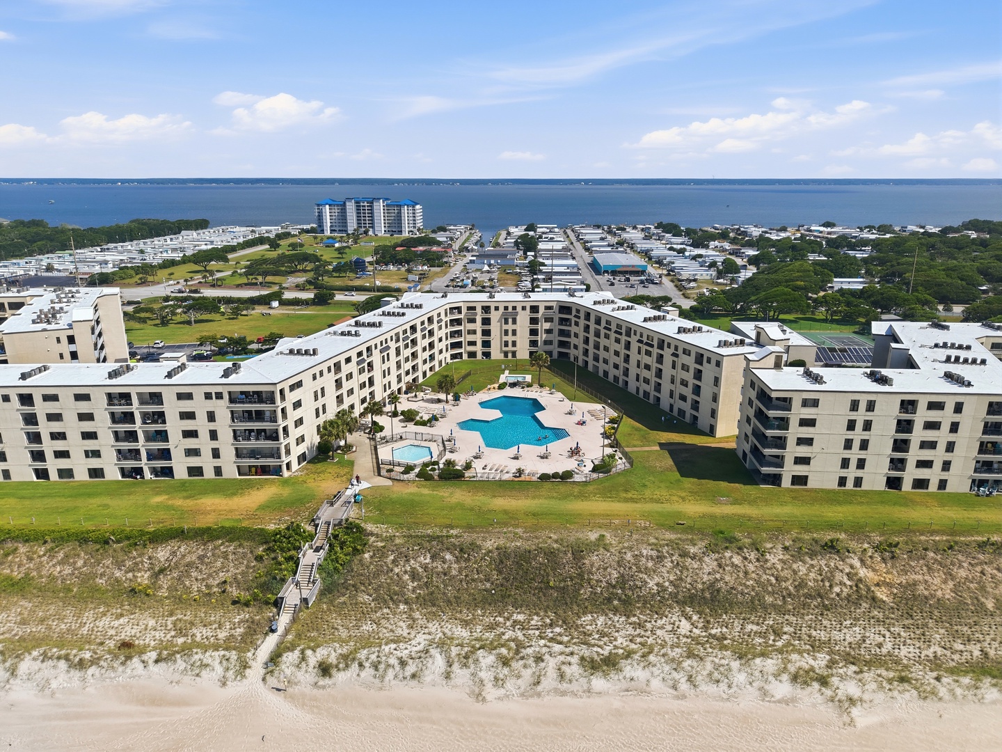 Beachfront vacation rental property featuring a central pool courtyard, direct beach access via boardwalk, and expansive bay views on a scenic coastal stretch.