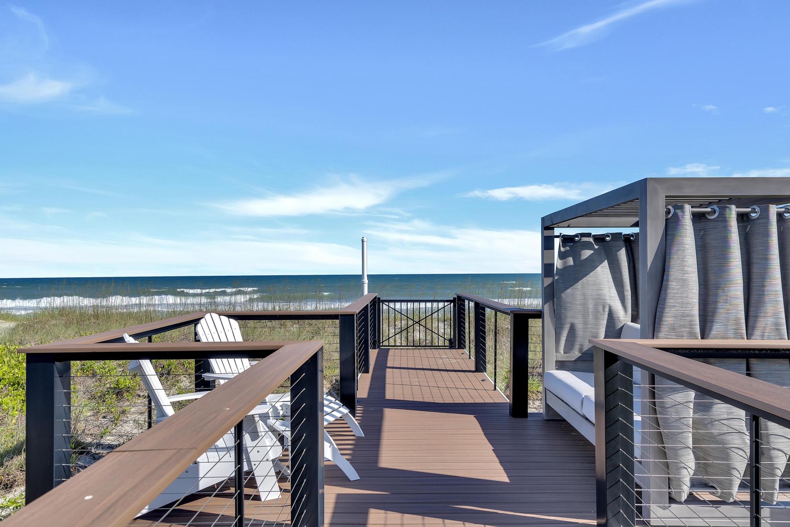 A private deck leads directly to the sandy shoreline, where white Adirondack chairs await and a shaded cabana offers a cool retreat after hours in the sun.