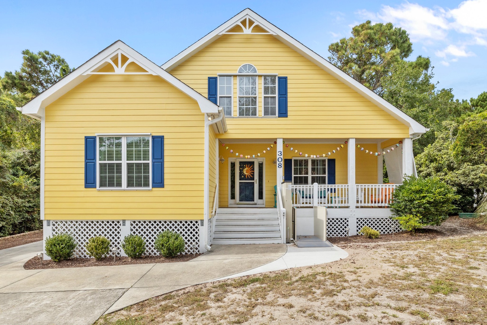 Cheerful yellow cottage with blue shutters and welcoming front porch featuring string lights and white railings.