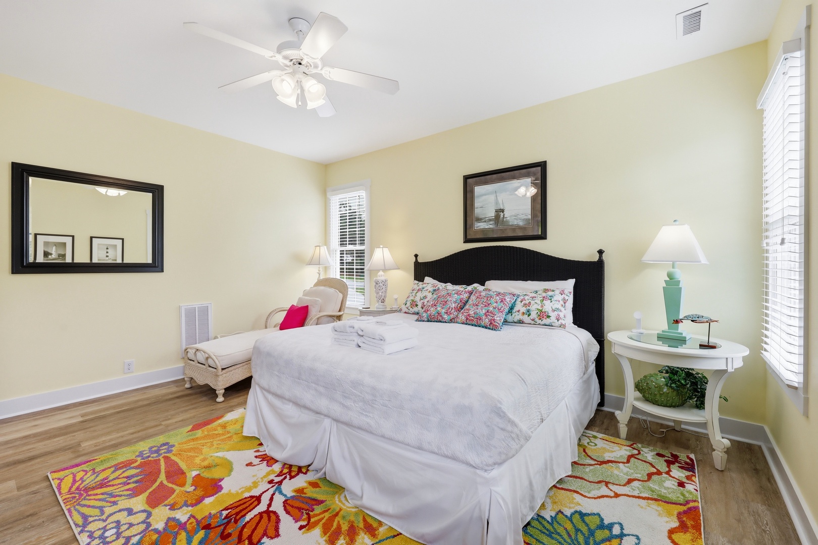 Settle into your bright coastal bedroom with plush linens, cheerful tropical accents, and gentle breezes from the ceiling fan above. A peaceful space to rest and recharge.