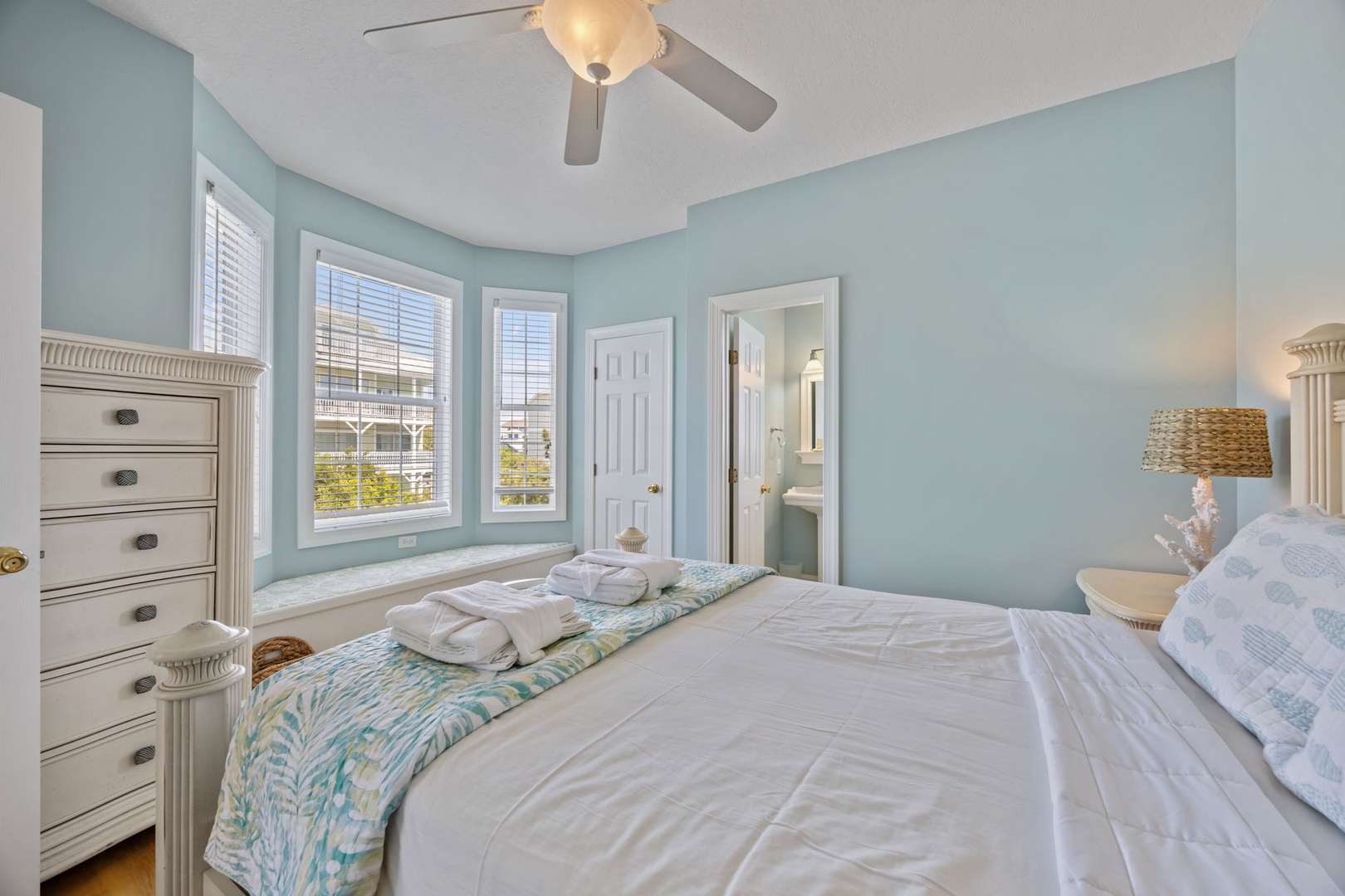Drift off in this serene bedroom with soft blue walls, crisp linens, and a gentle ceiling fan creating the perfect coastal retreat atmosphere.
