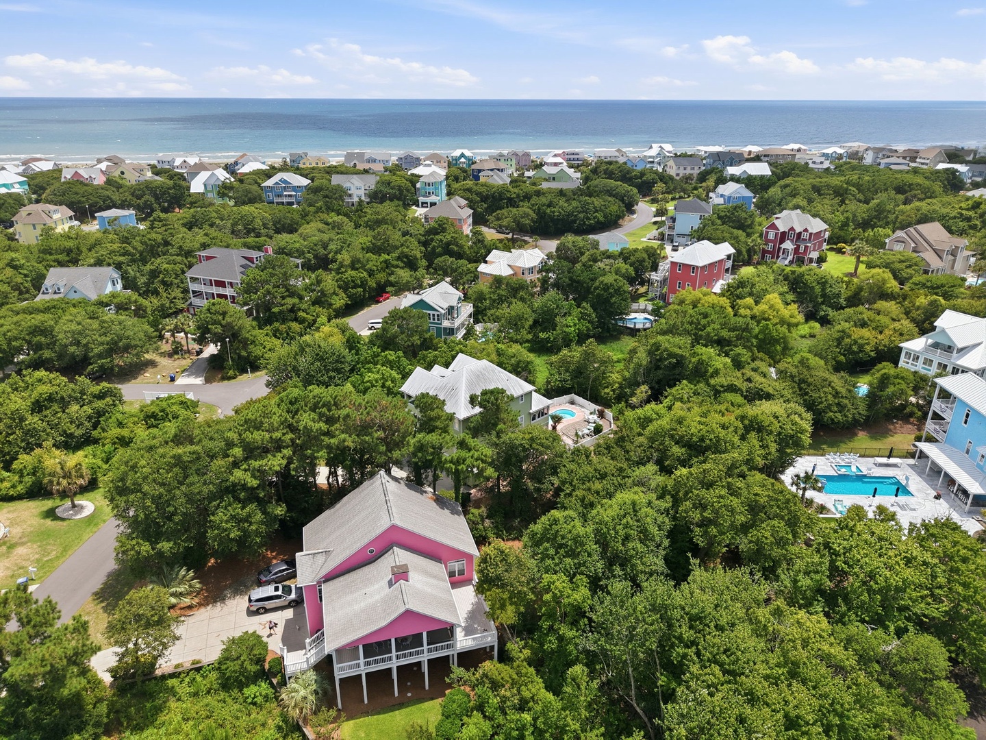 Aerial view showcasing the coastal community with beach access, vacation homes nestled among lush greenery, and the ocean visible in the distance.