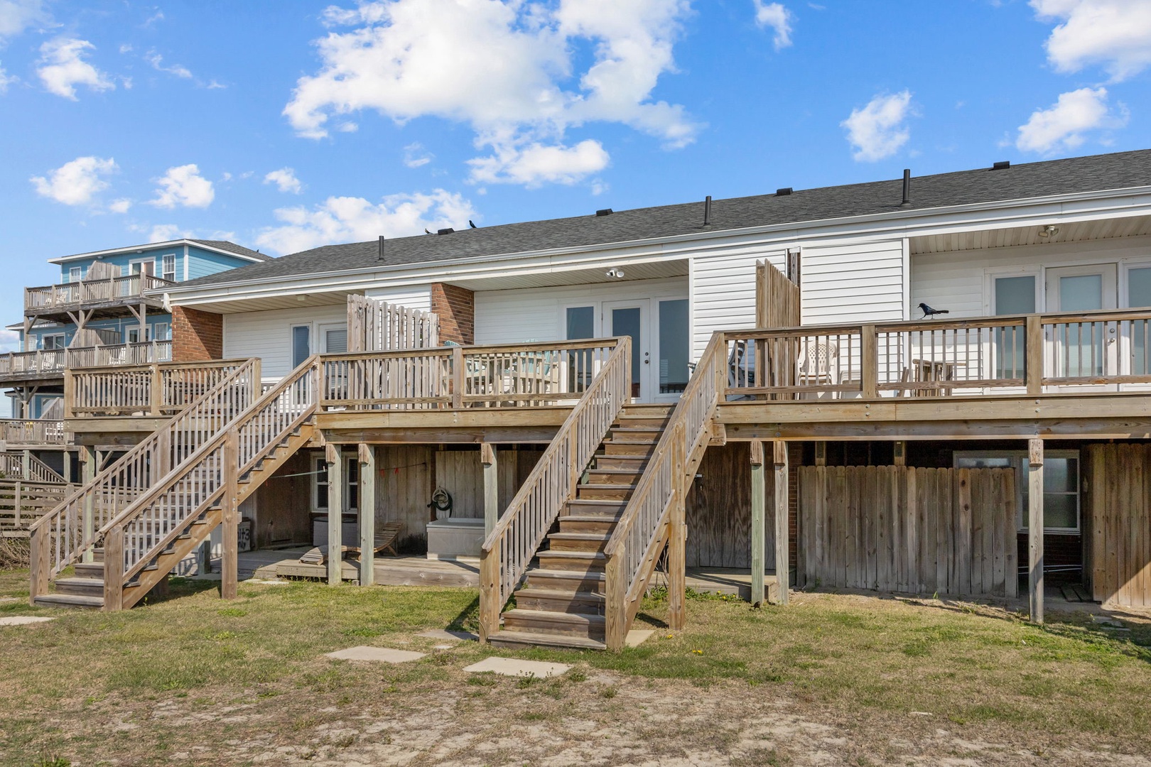 Coastal vacation rental properties featuring elevated decks and wooden staircases under a bright blue sky.