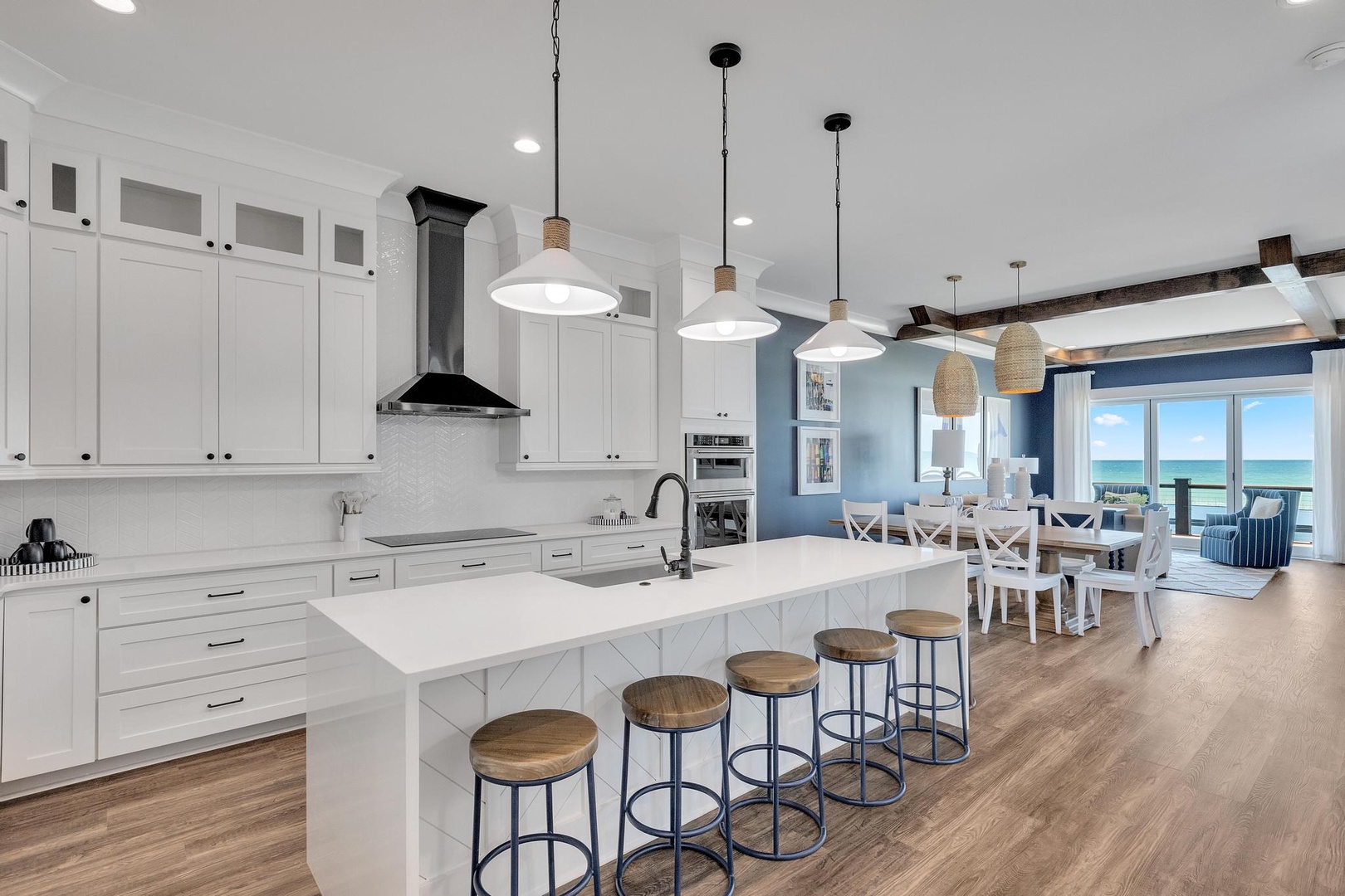 Step into your fully equipped kitchen with gleaming white cabinetry, expansive island seating, and an open layout flowing to the dining area where stunning ocean views await through floor-to-ceiling windows.