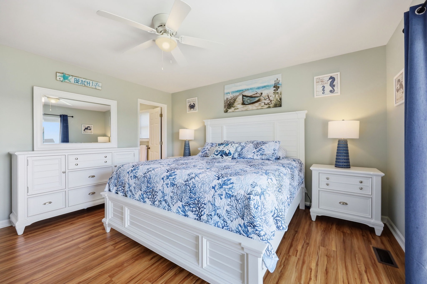 Drift off in this coastal-inspired bedroom where ocean blue bedding and crisp white furnishings create your serene seaside escape beneath the gentle breeze of a ceiling fan.