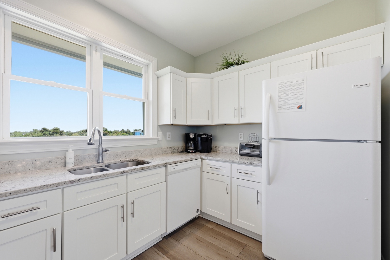 Your bright, fully-equipped kitchen invites you to brew morning coffee while natural light pours through large windows overlooking peaceful treetops. White cabinetry and granite counters create a fresh, inviting space.