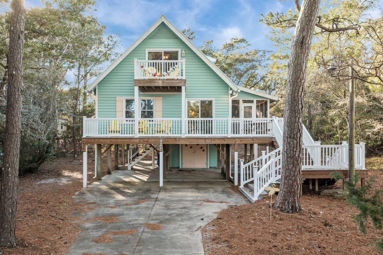 Charming coastal cottage with wraparound deck and convenient parking beneath, nestled among mature trees.