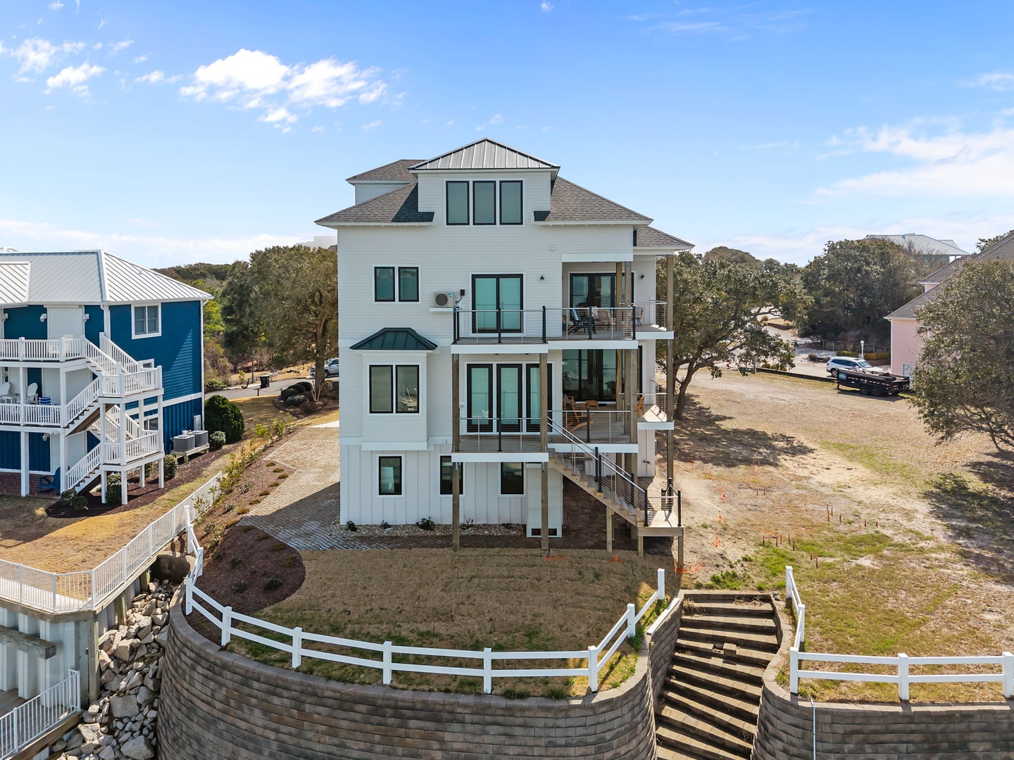 Modern four-story beach house with elevated design surrounded by coastal community and mature oak trees.